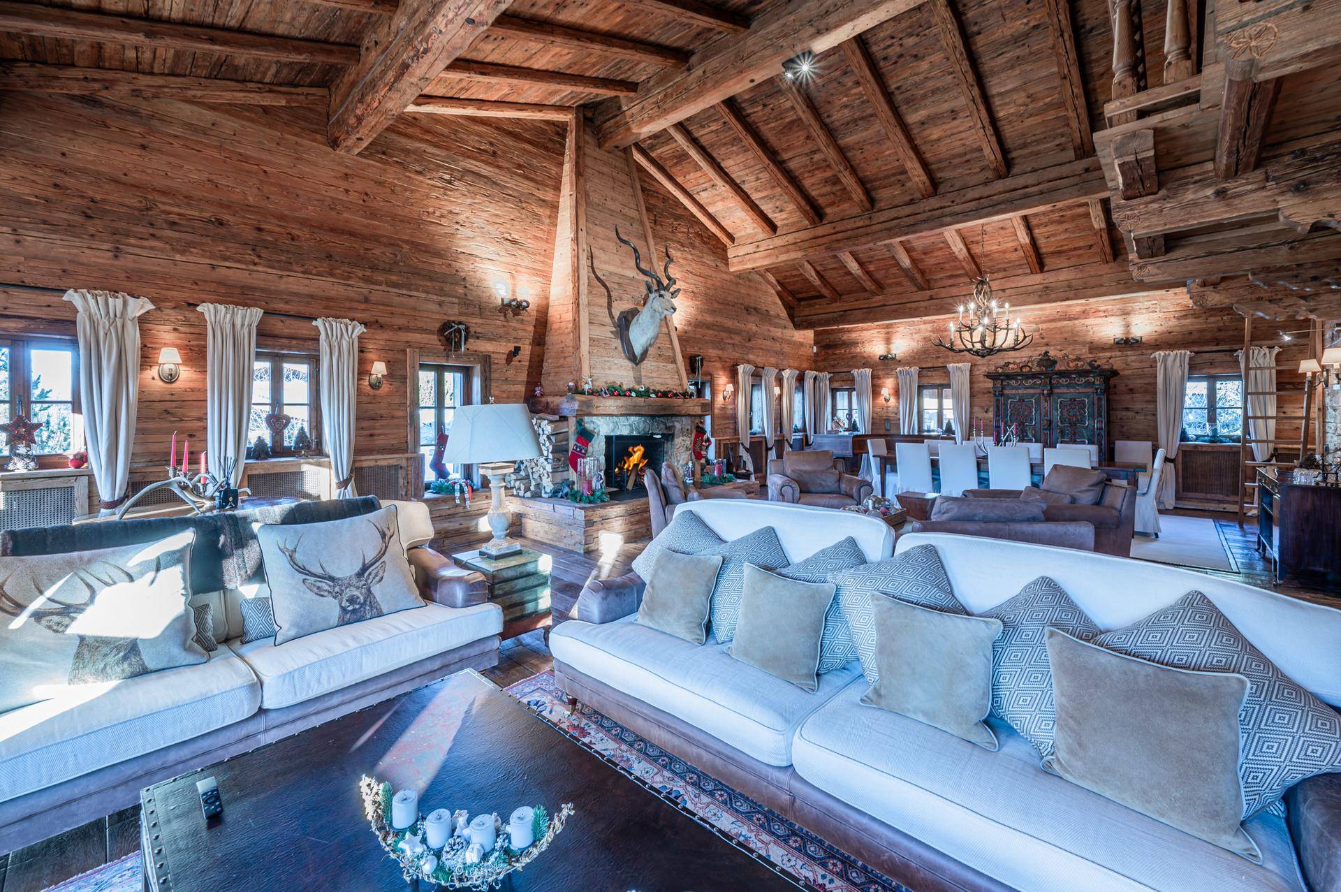 Geräumiges Wohnzimmer im alpinen Stil mit Holzbalken, Kamin und gemütlichen Sofas.