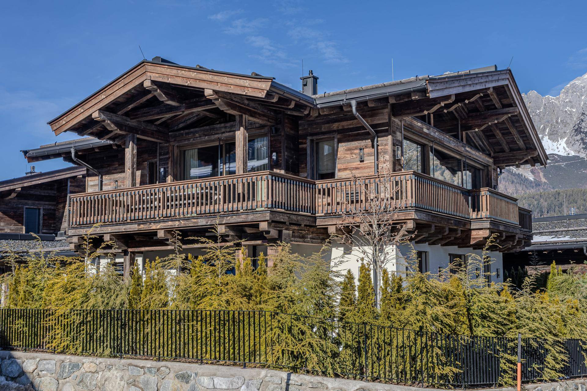 Traditionelles Holzchalet mit mehreren Balkonen und Bergblick unter blauem Himmel.