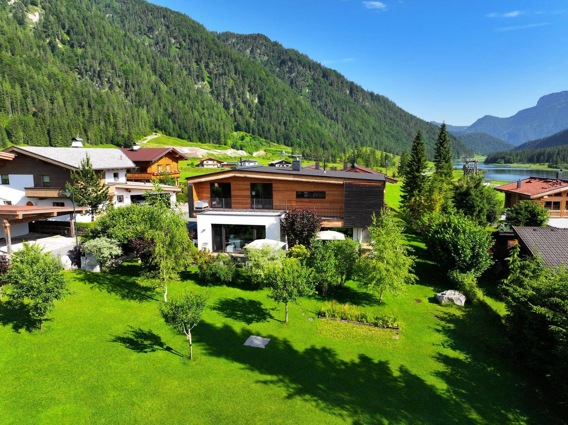 Panoramablick auf ein modernes Wohnhaus eingebettet in eine grüne Alpenlandschaft.