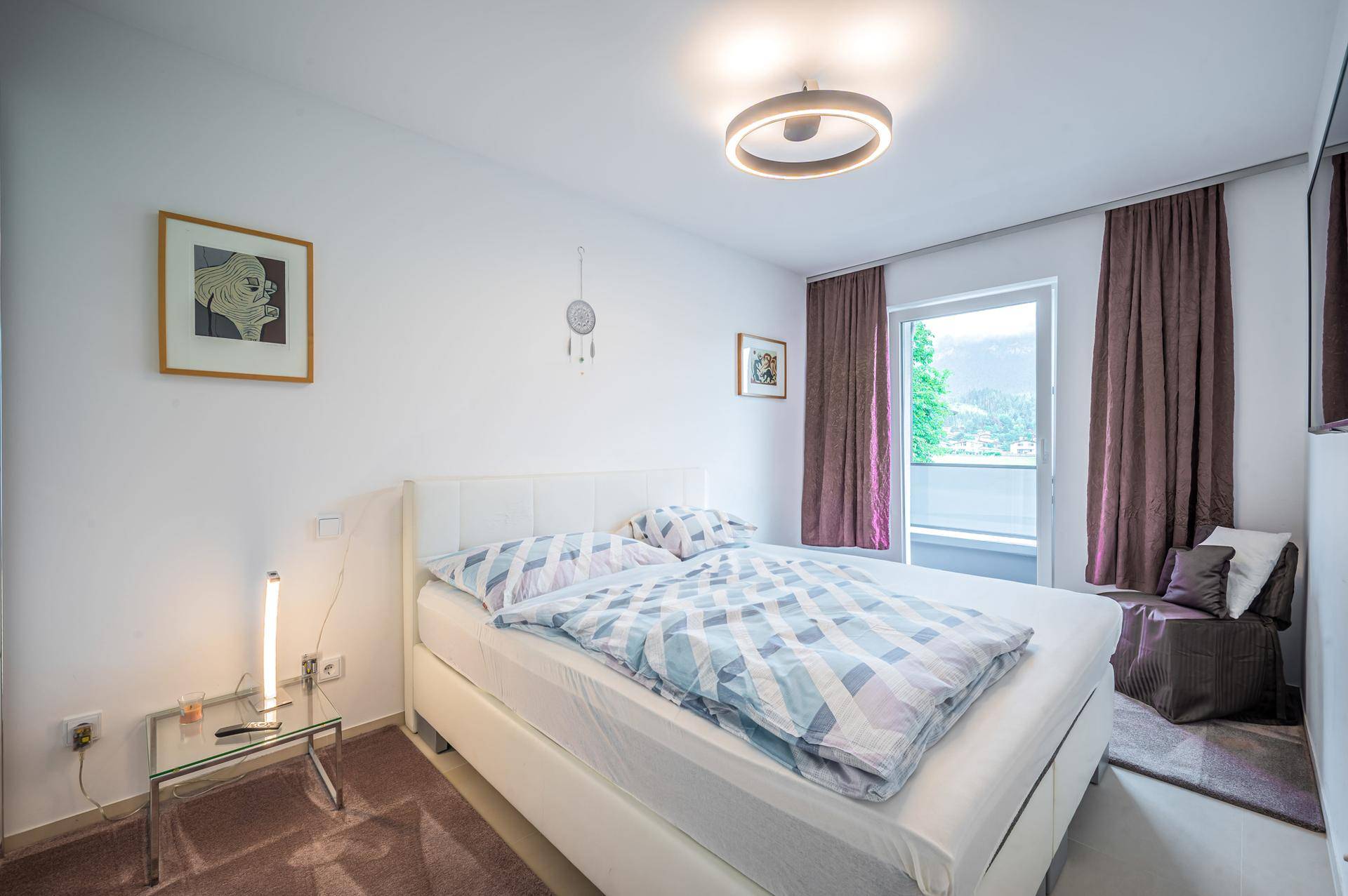 Helles Schlafzimmer mit Doppelbett, schlichter Einrichtung und Fenster mit Blick ins Grüne.