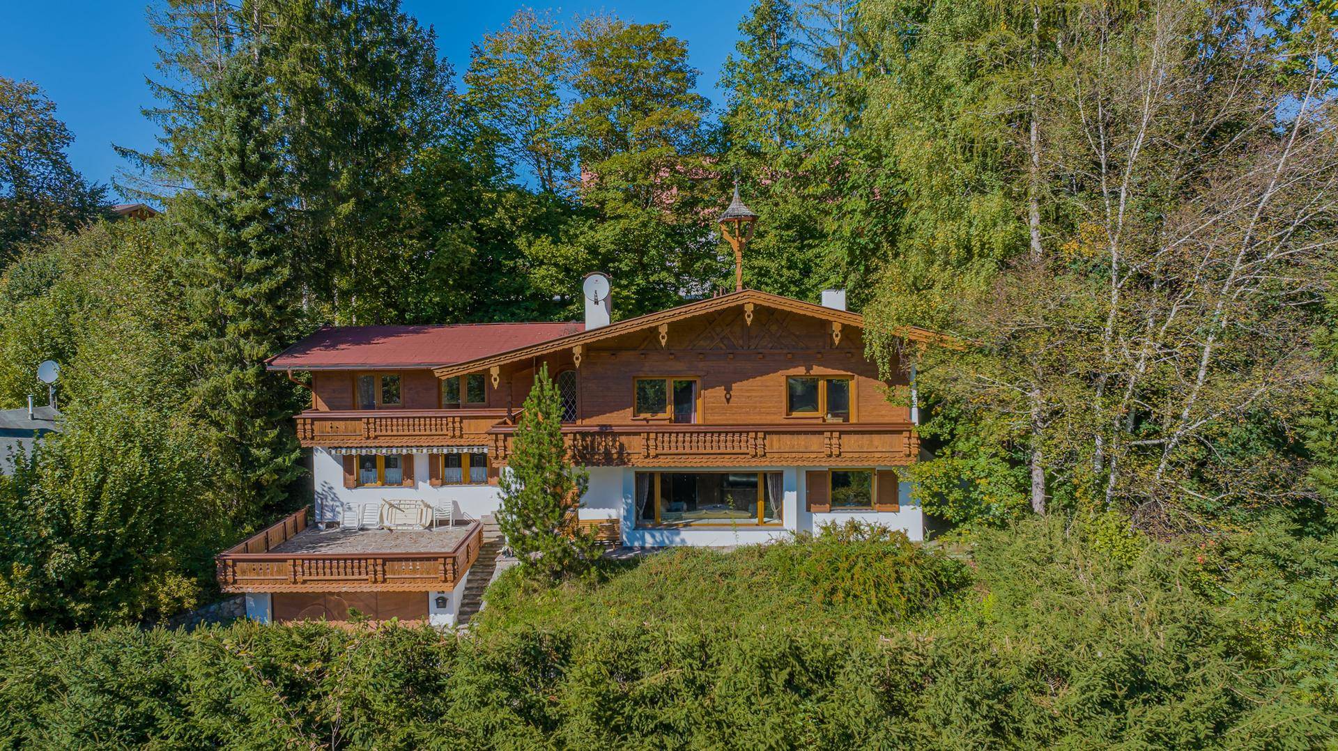 Traditionelles Holzchalet umgeben von üppigem Grün und hohen Bäumen, mit mehreren Balkonen und einer Terrasse.
