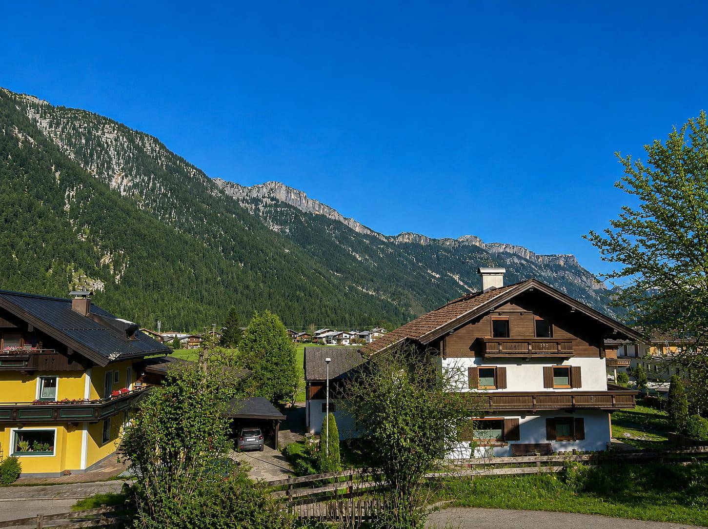 Alpenländliche Häuser in einem Dorf mit beeindruckendem Bergpanorama im Hintergrund.