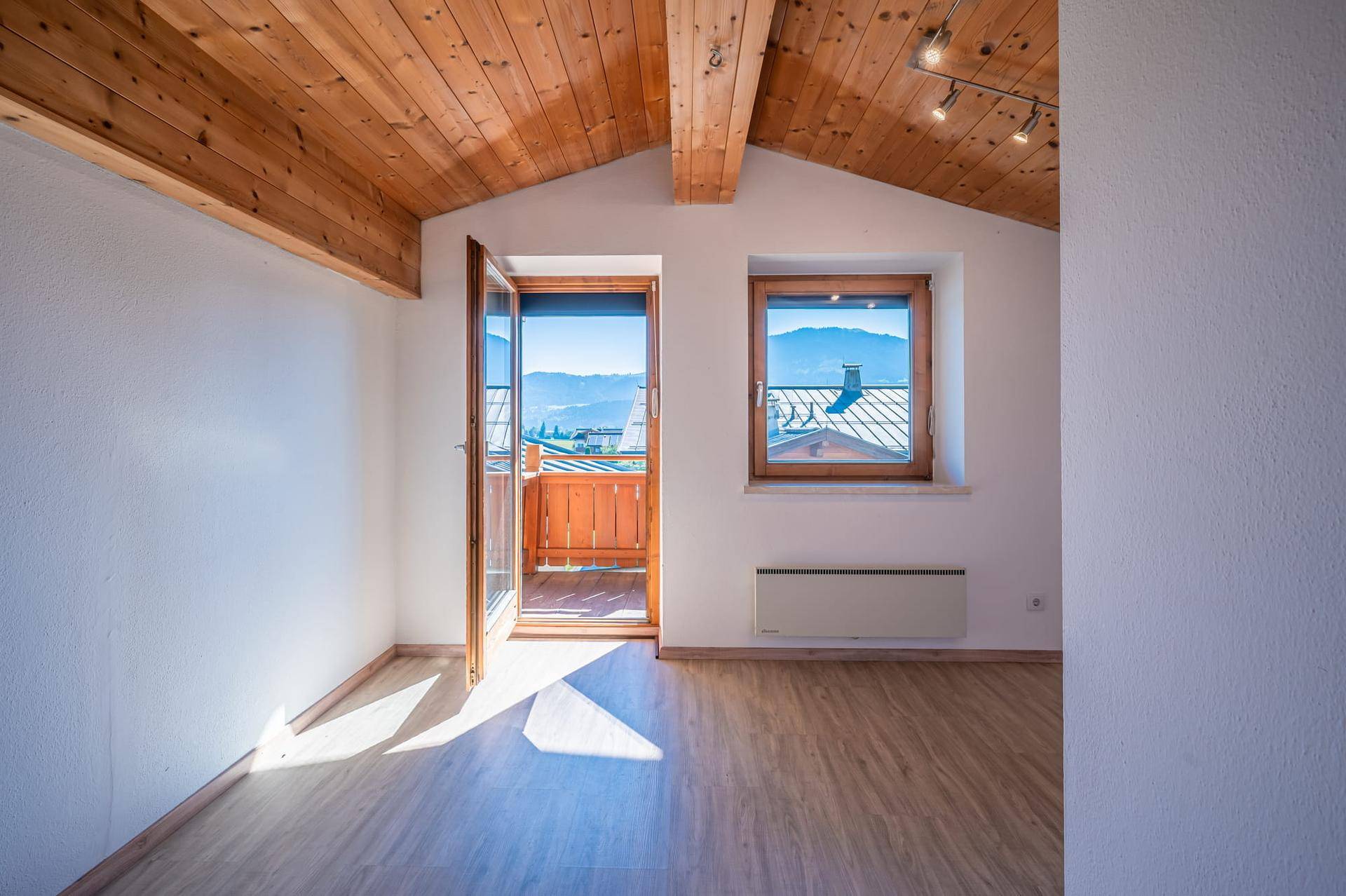 Heller Raum mit Holzbalkendecke, Zugang zu einem französischen Balkon und Bergblick.