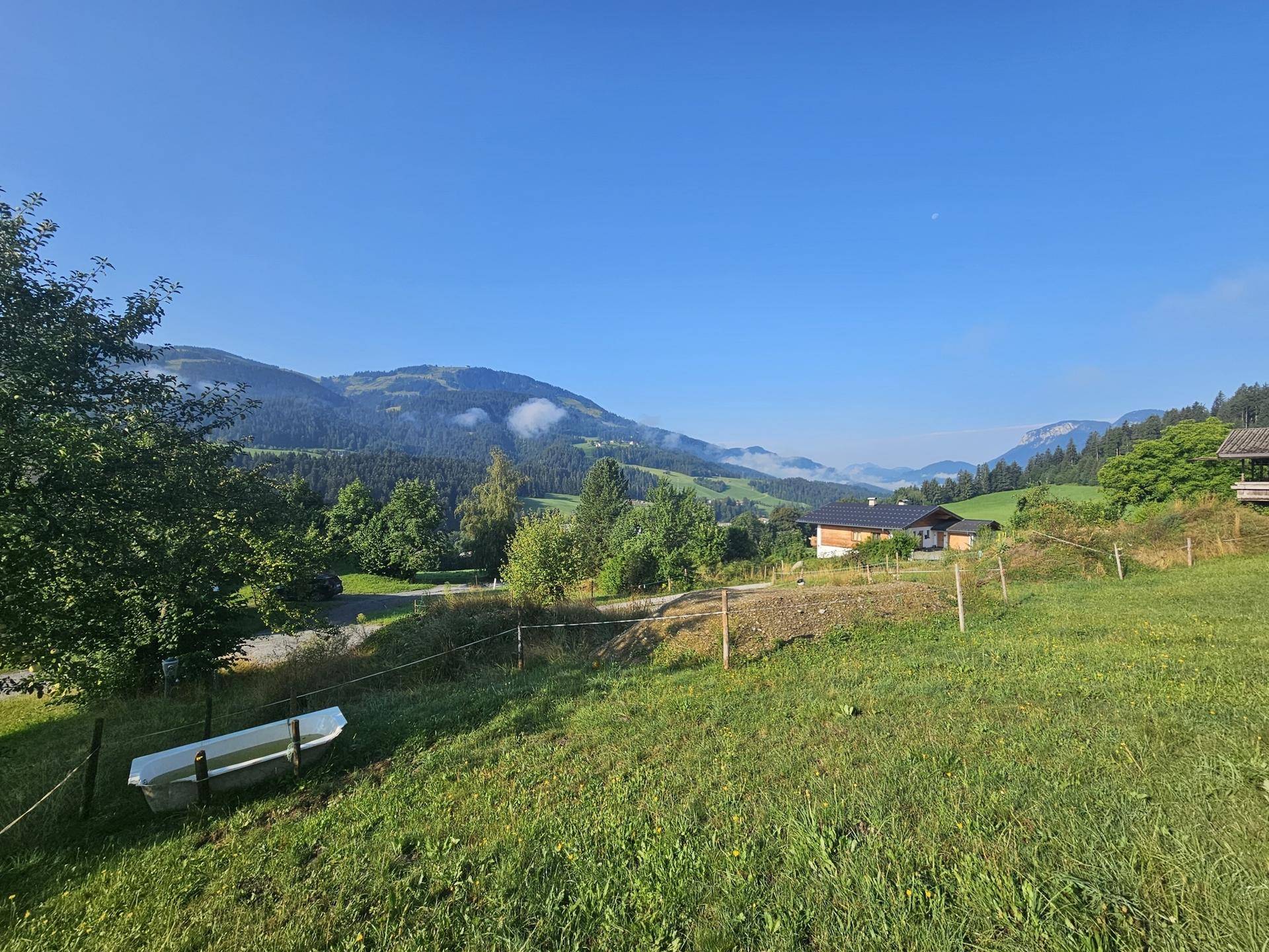 Haus in idyllischer Berglandschaft mit weitem Blick über grüne Hügel und Wälder unter blauem Himmel.