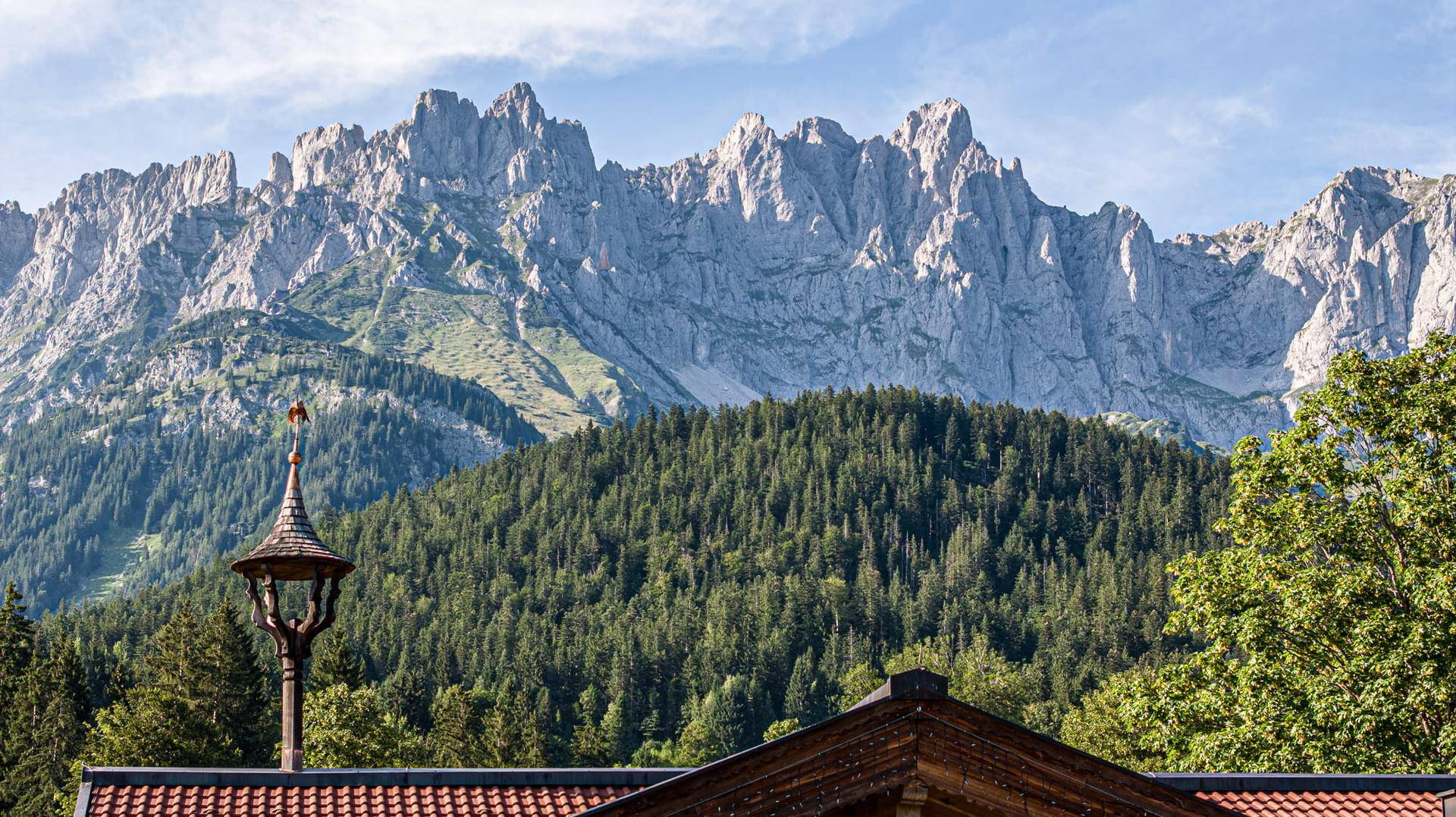 Spektakulärer Blick auf die schroffen Berggipfel über dem traditionellen Dach eines Alpenhauses.