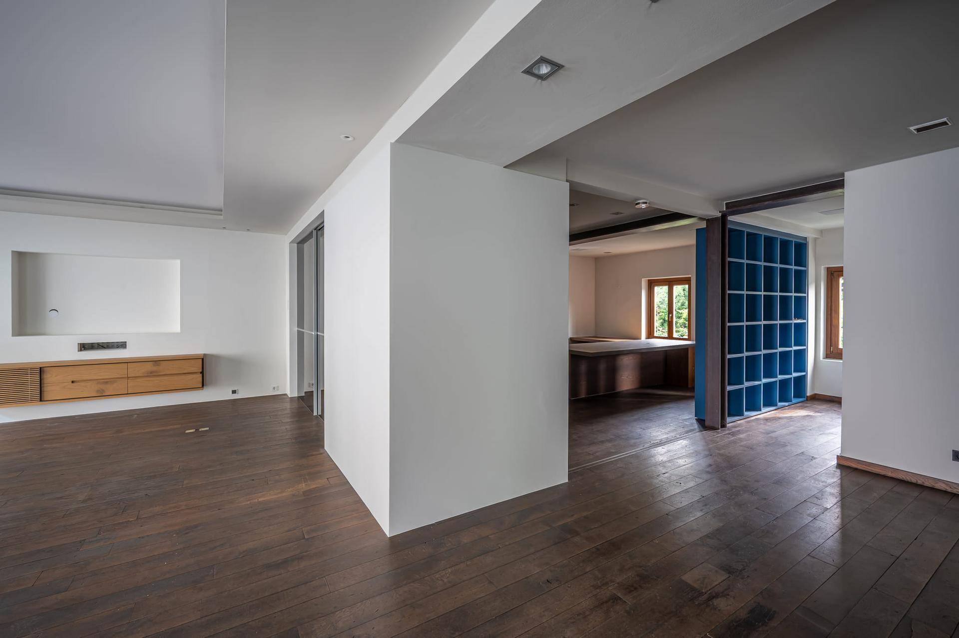 Heller Innenraum mit dunklem Holzboden, weißen Wänden, einem Einbauregal und einem blauen Raumteiler.
