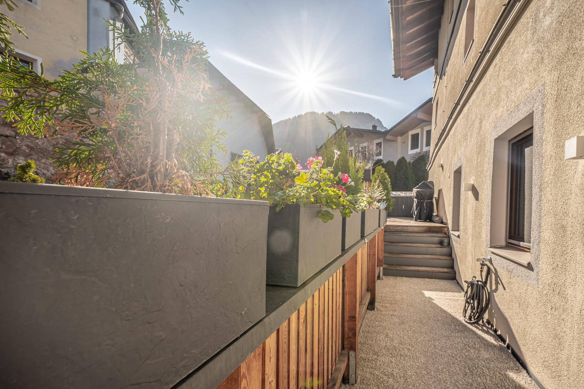 Sonniger Außenbereich mit Pflanzenkübeln und Treppe, umgeben von traditioneller Architektur und Bergblick.