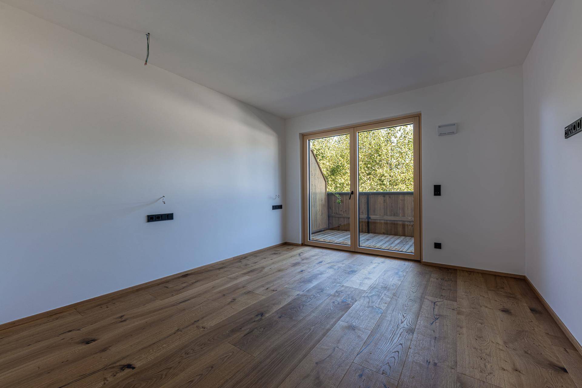 Heller Raum mit Holzboden und Schiebetür, die Zugang zu einem Balkon bietet.