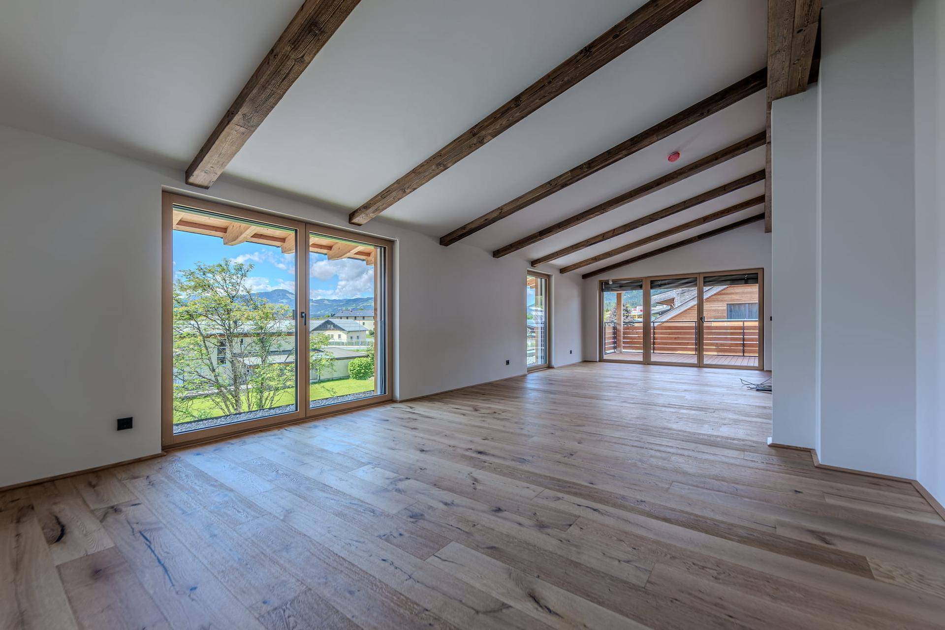 Heller Wohnbereich mit großen Fenstern, Holzbalken und Bergblick, ideal für entspanntes Wohnen.