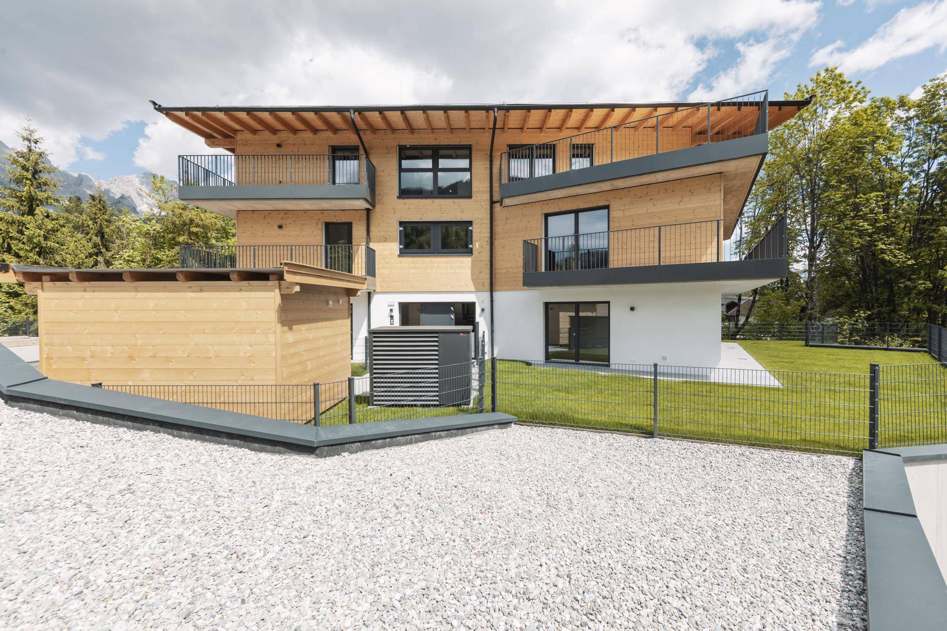 Moderne Architektur des Gebäudes mit Holzfassade, Balkonen und gepflegter Außenanlage.