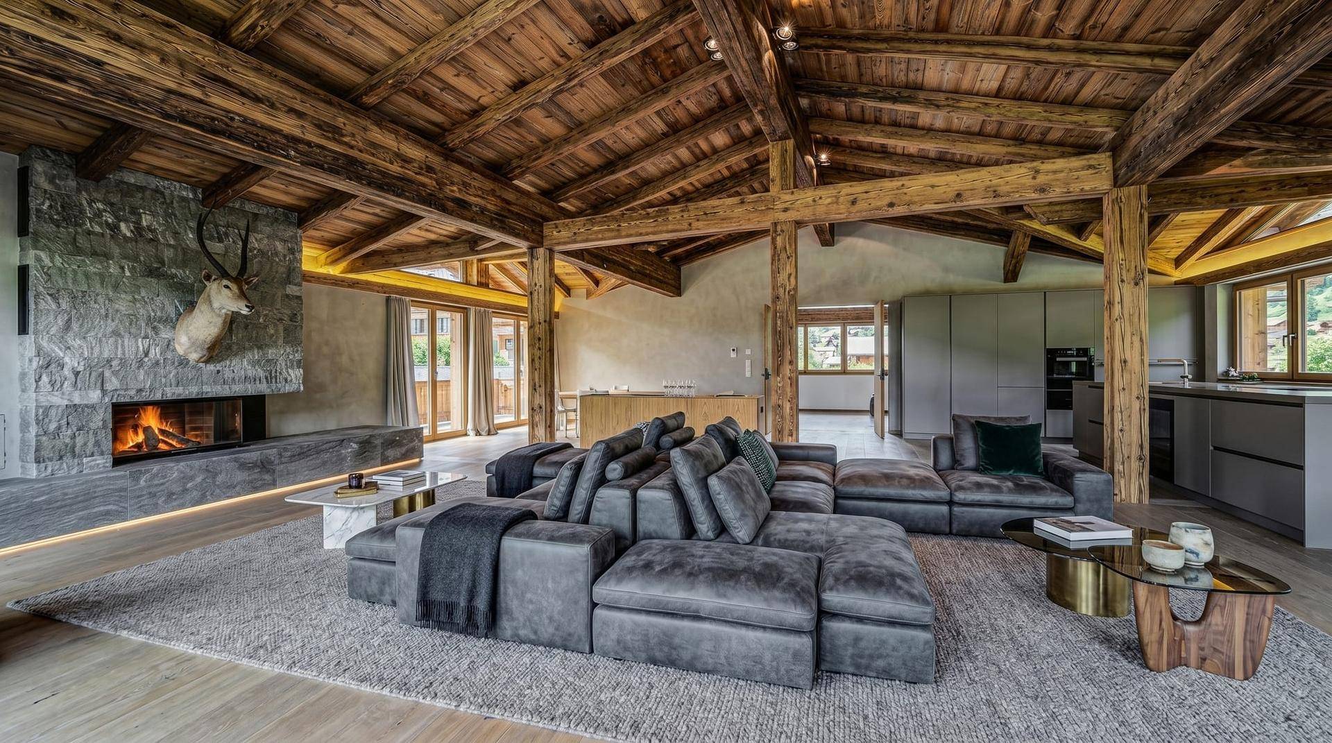Geräumiger, offener Wohnbereich mit rustikalen Holzbalken, modernem Sofa und Steinkamin.