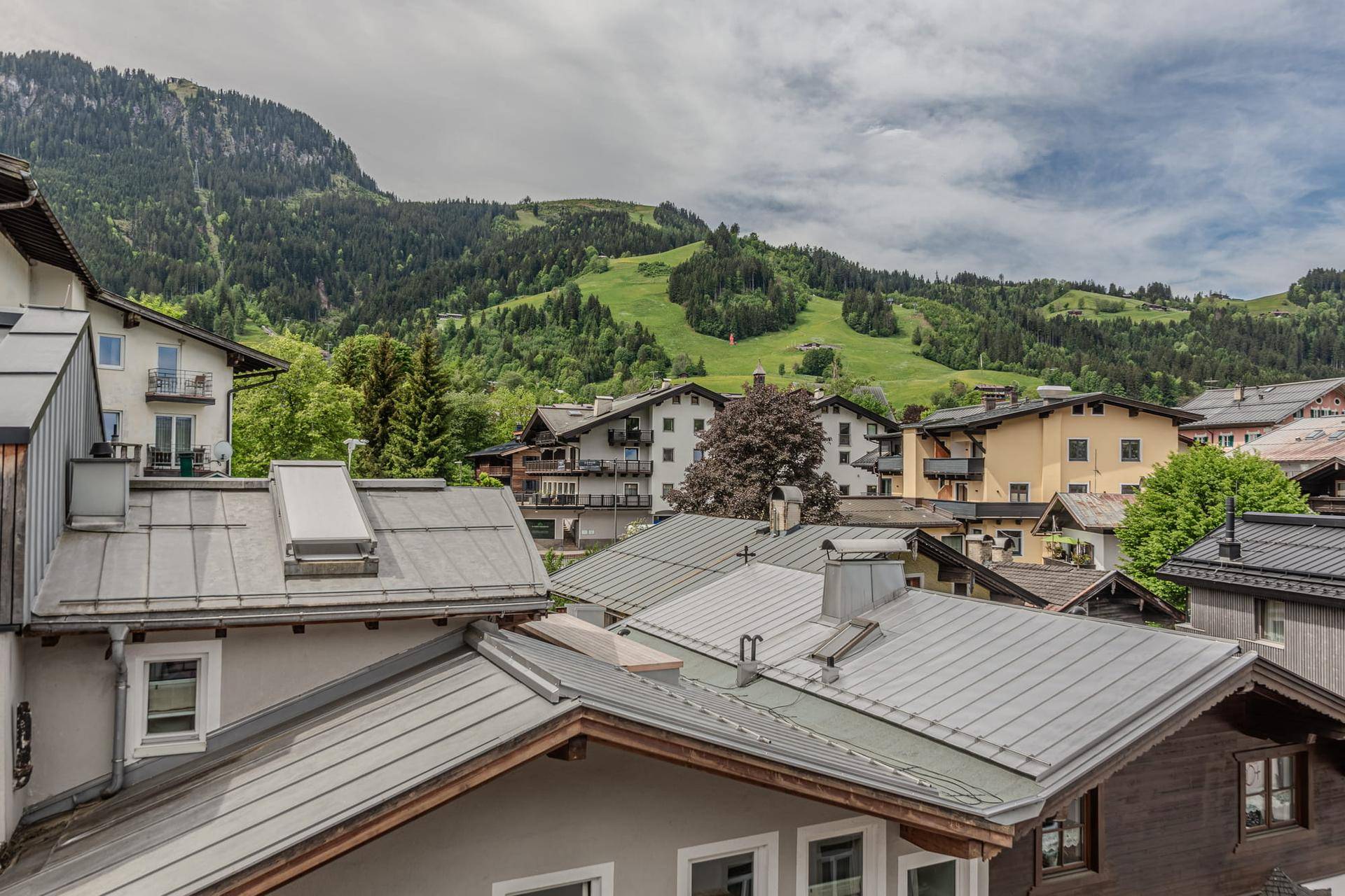 Panoramablick über die Dächer eines Bergdorfes mit grünen Hängen und Bergen im Hintergrund.