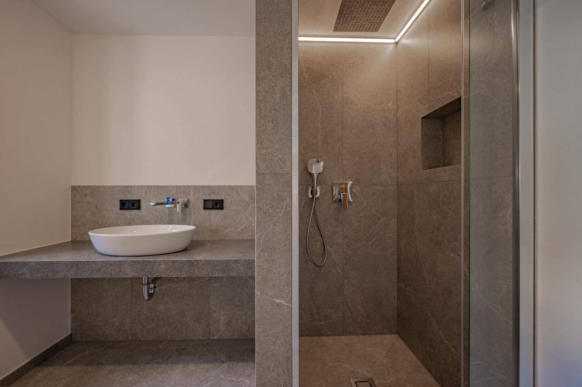 Modernes Badezimmer mit großformatigen Fliesen, Aufsatzwaschbecken und Regendusche.