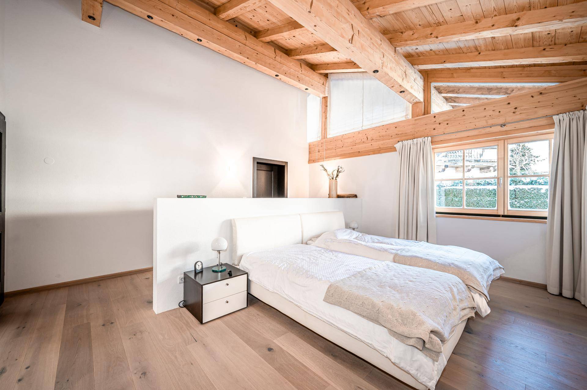 Helles Schlafzimmer mit Holzbalkendecke, großem Doppelbett und Blick ins Grüne.