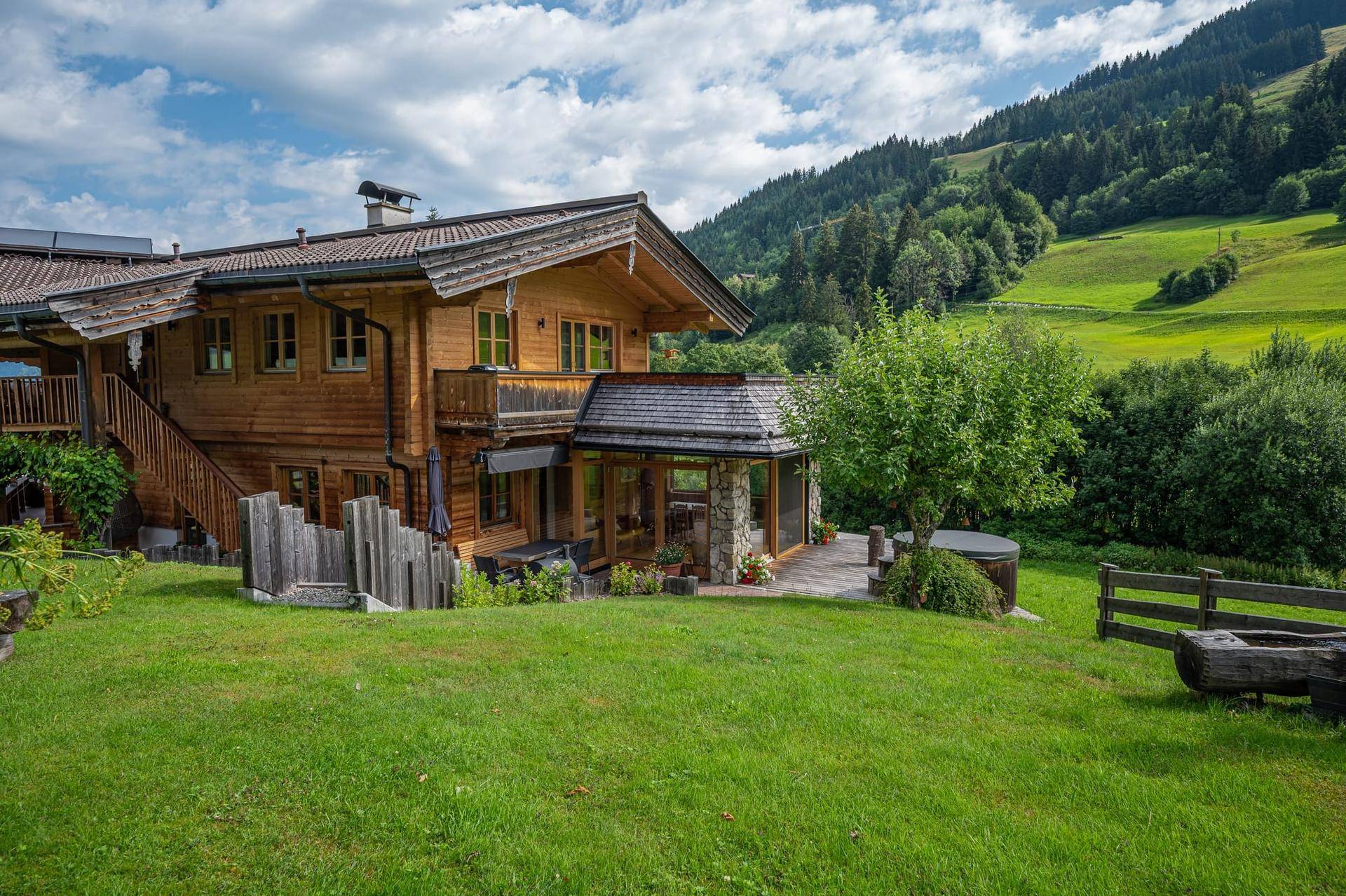 Charmantes Holzhaus im Grünen mit weitläufigem Garten und Bergblick unter blauem Himmel.