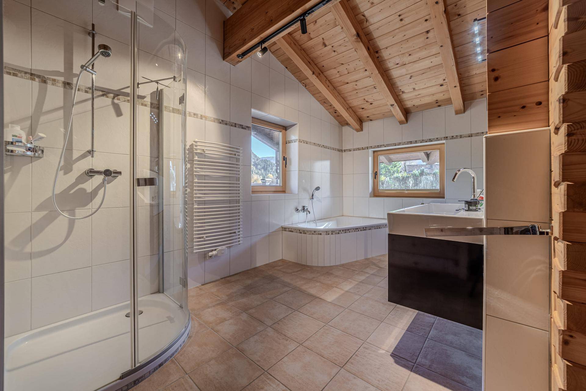 Modernes Badezimmer mit Dusche, Eckbadewanne, Fliesenboden und Holzbalkendecke.