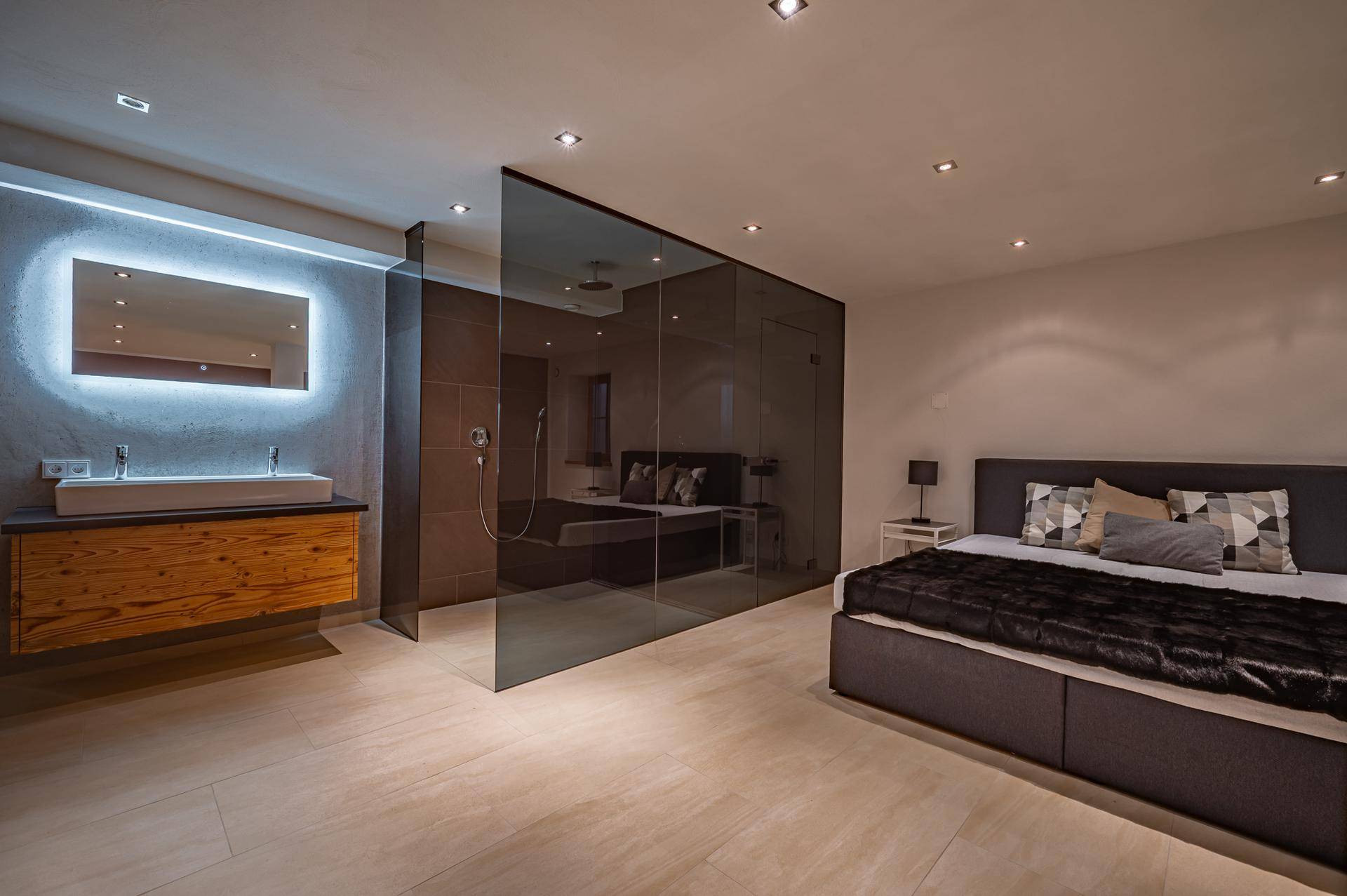 Schlafzimmer mit integriertem Badbereich, modernem Waschbecken und begehbarer Dusche hinter Glaswand.