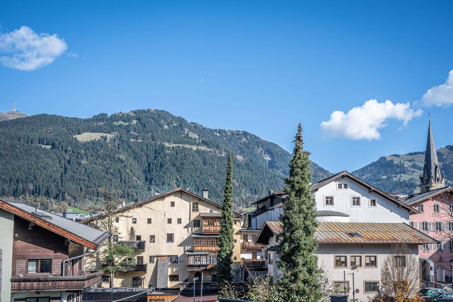 Panoramablick auf das charmante Alpendorf und die umliegenden grünen Berge unter blauem Himmel.