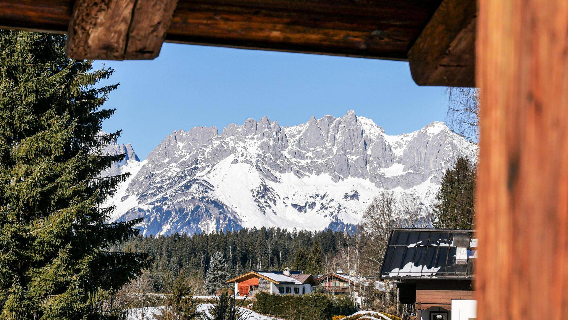 Spektakulärer Blick auf schneebedeckte Berge und Wälder unter klarem, blauem Himmel.