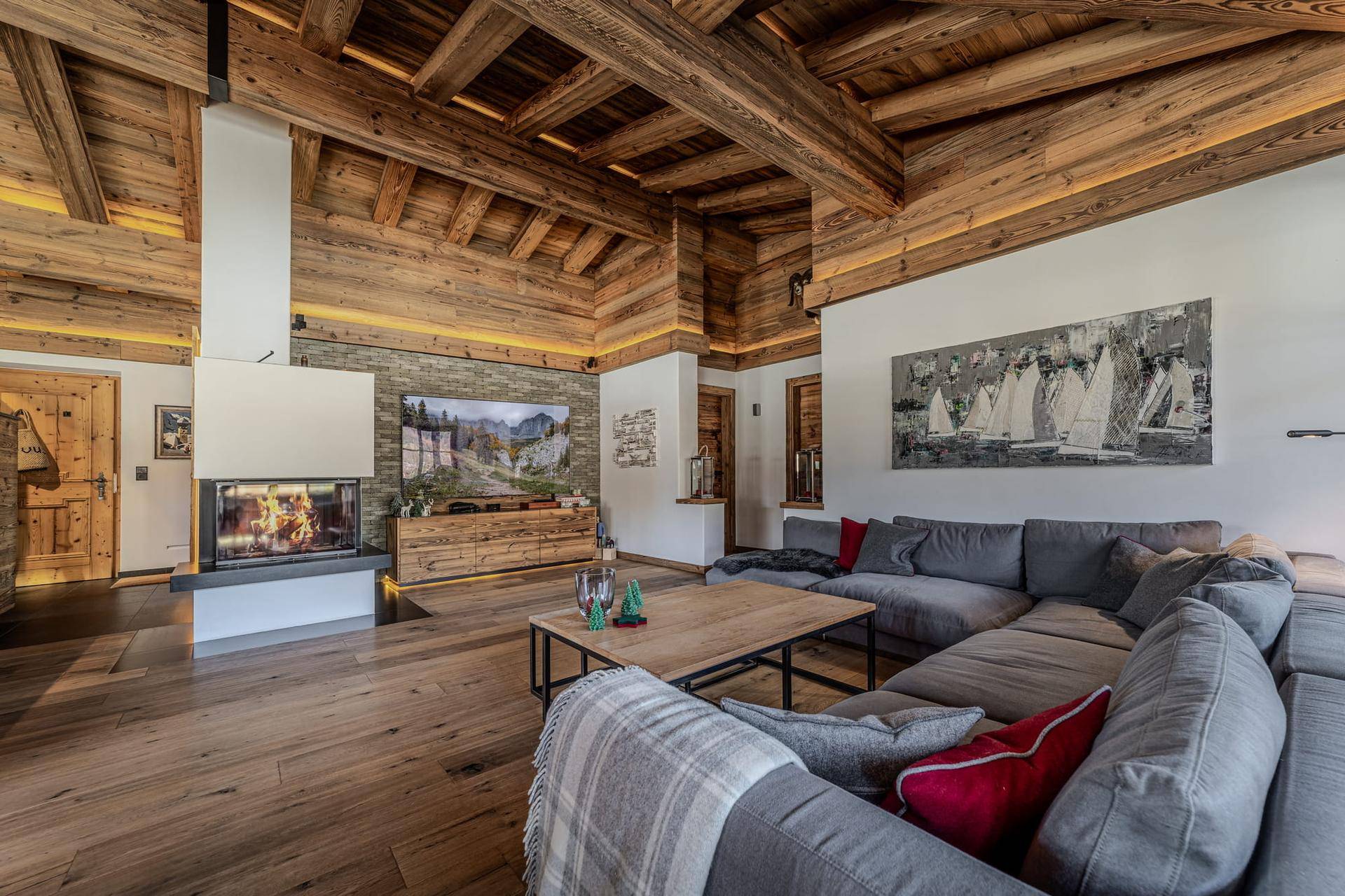 Geräumiges Wohnzimmer mit modernem Kamin, bequemer Sitzecke und beeindruckender Holzbalkendecke.