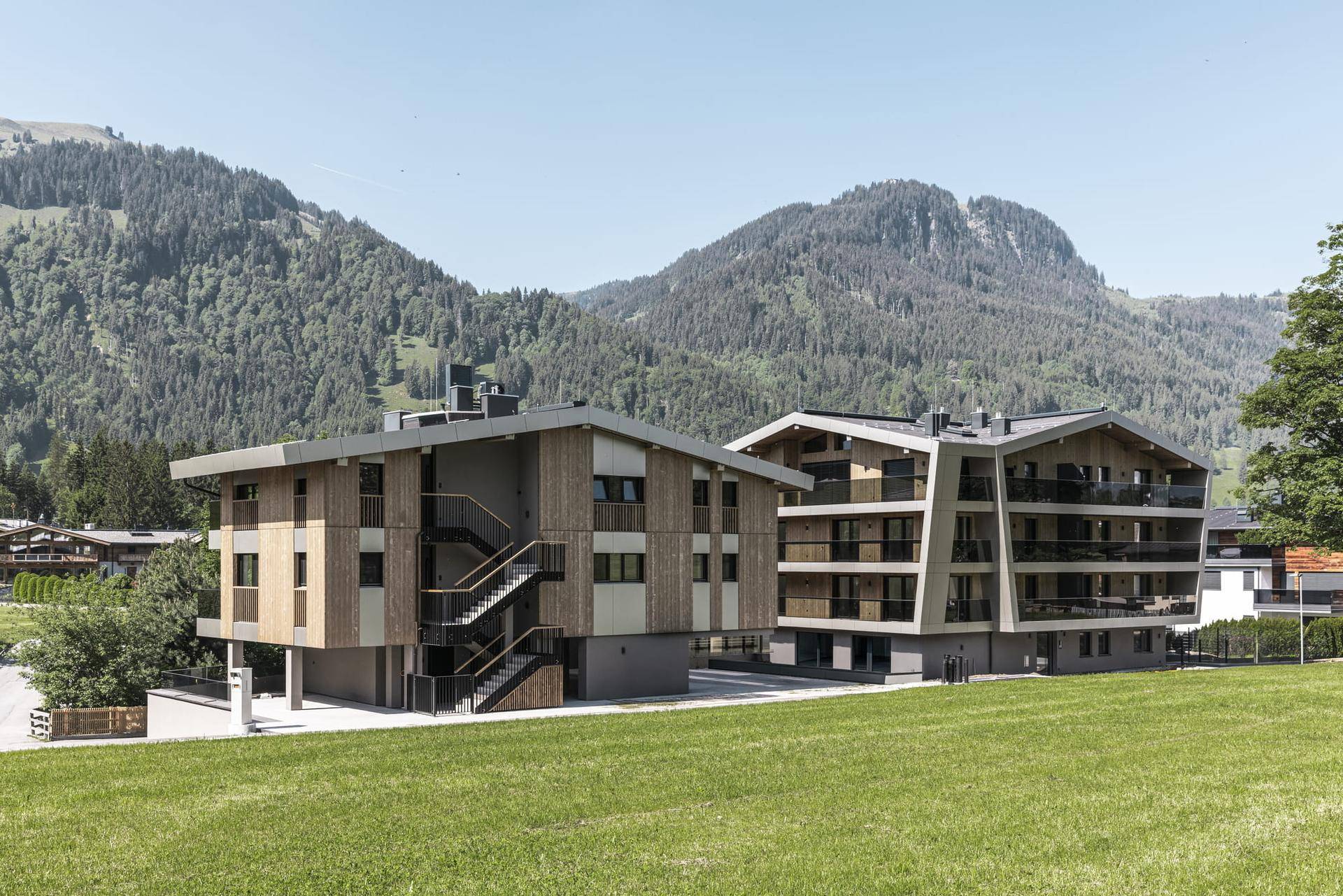 Zwei moderne Gebäude in alpiner Umgebung mit Holzfassaden und Bergblick.