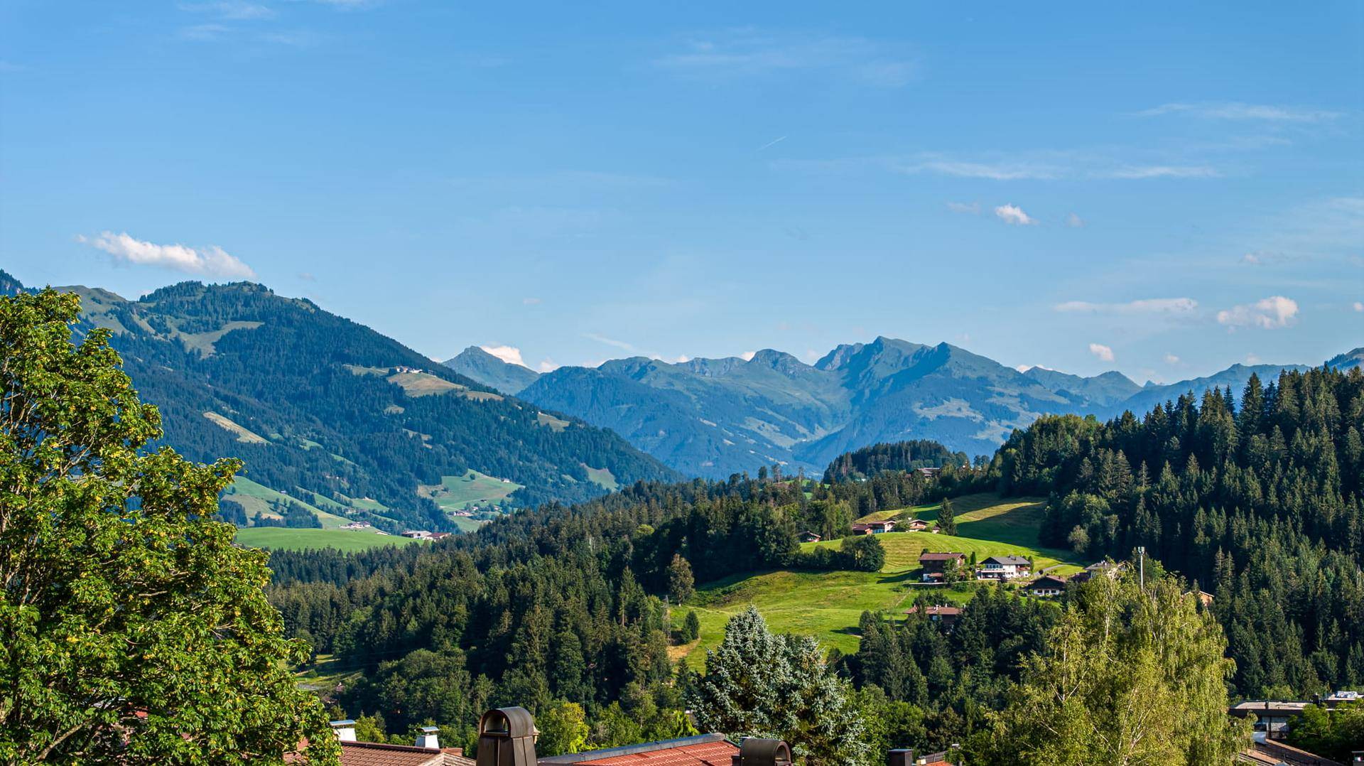 Weitläufiger Panoramablick auf die majestätische Berglandschaft und grüne Täler unter blauem Himmel.