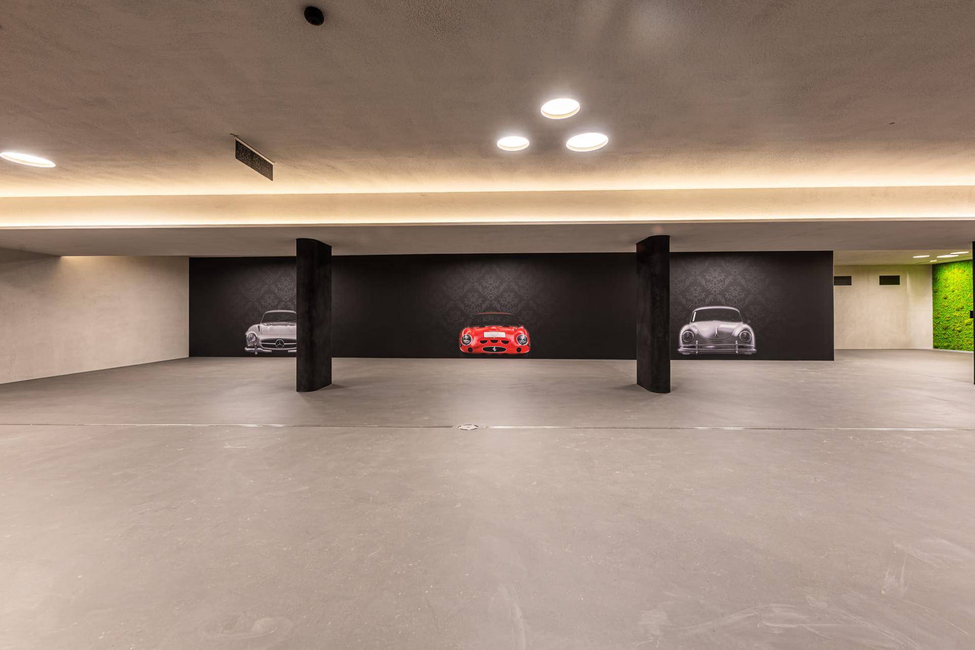 Geräumige Tiefgarage mit modernen Leuchten und dekorativen Wandbildern von klassischen Sportwagen.
