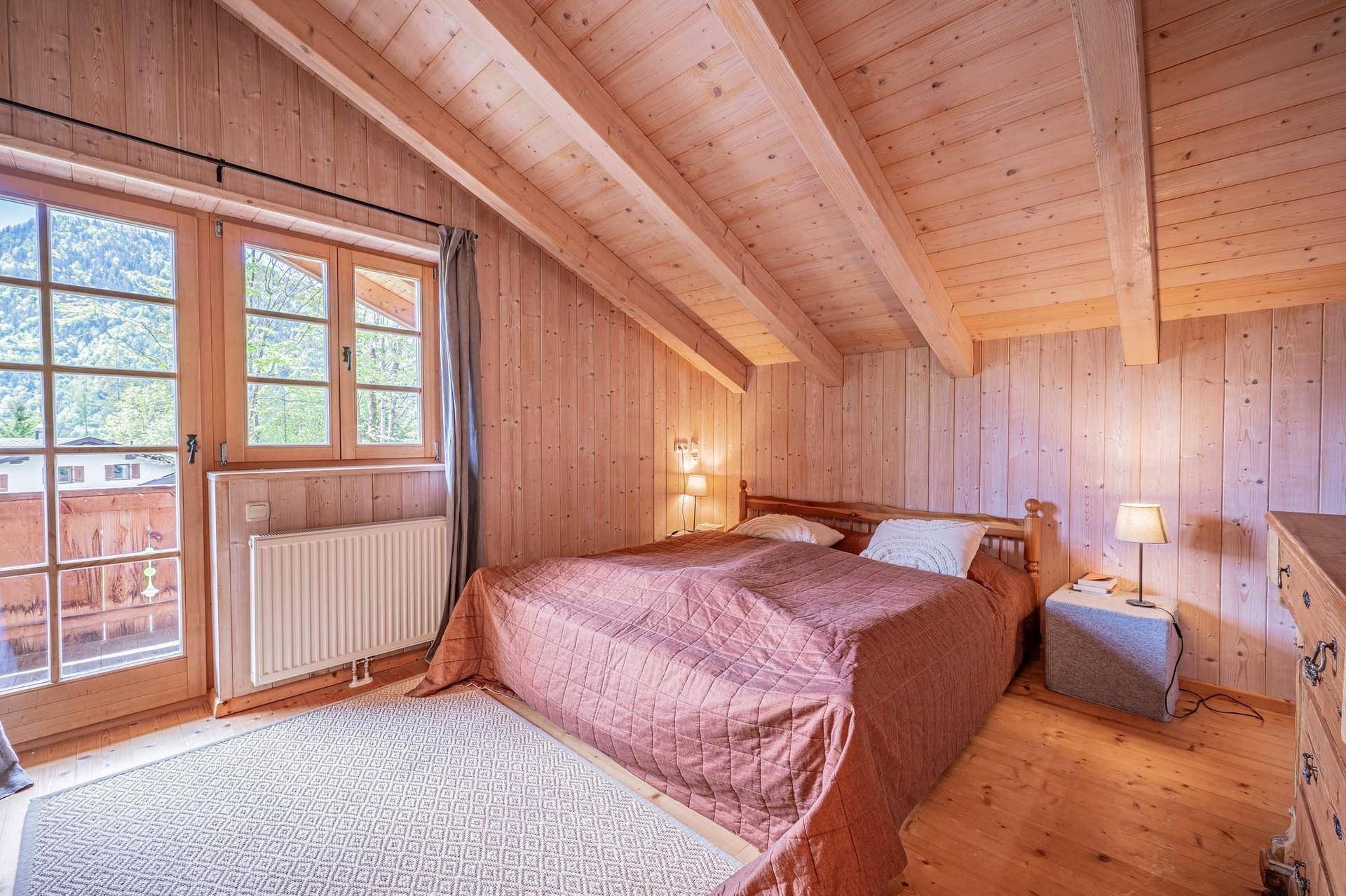 Helles Schlafzimmer mit Holzwänden, Dachschräge und Zugang zu einem Balkon.