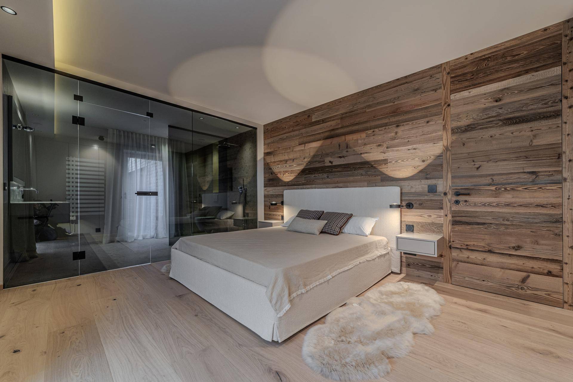 Elegantes Schlafzimmer mit Holzwand, Parkettboden und integriertem Badezimmer hinter Glaswänden.