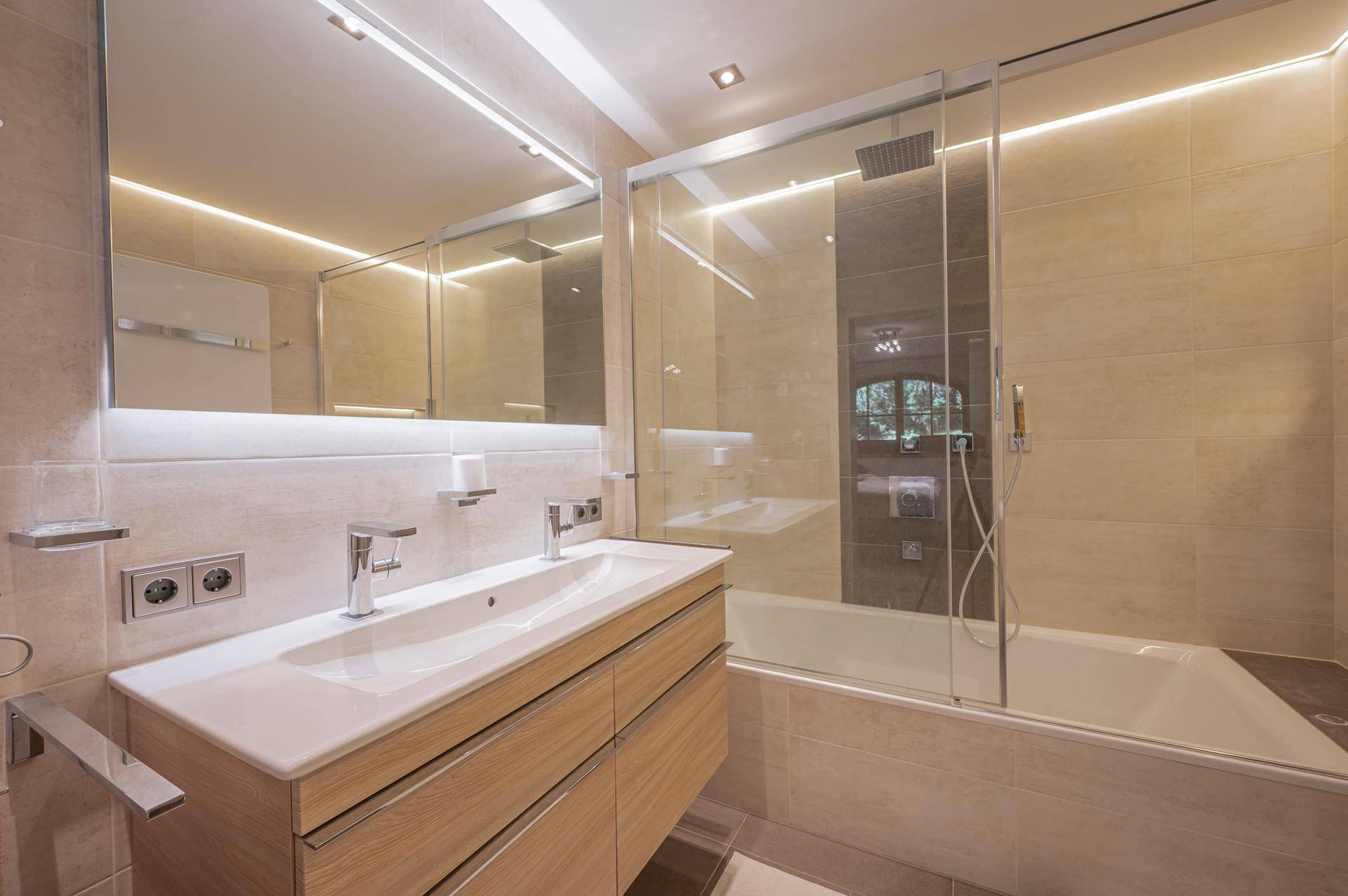Modernes Badezimmer mit Doppelwaschbecken, Badewanne und Duschabtrennung aus Glas.