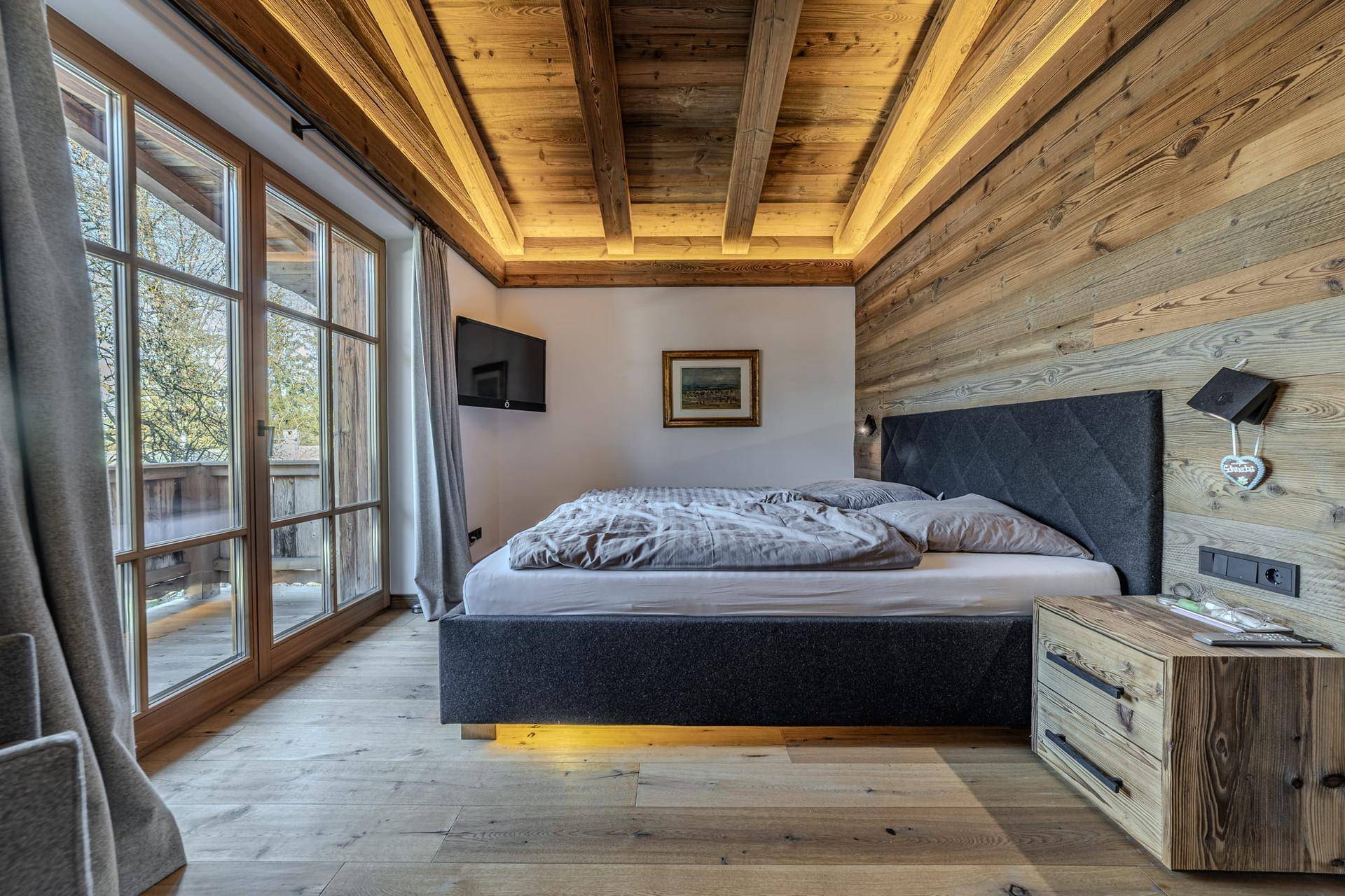 Gemütliches Schlafzimmer mit Holzwänden, Holzbalkendecke und Zugang zu einem Balkon oder einer Terrasse.