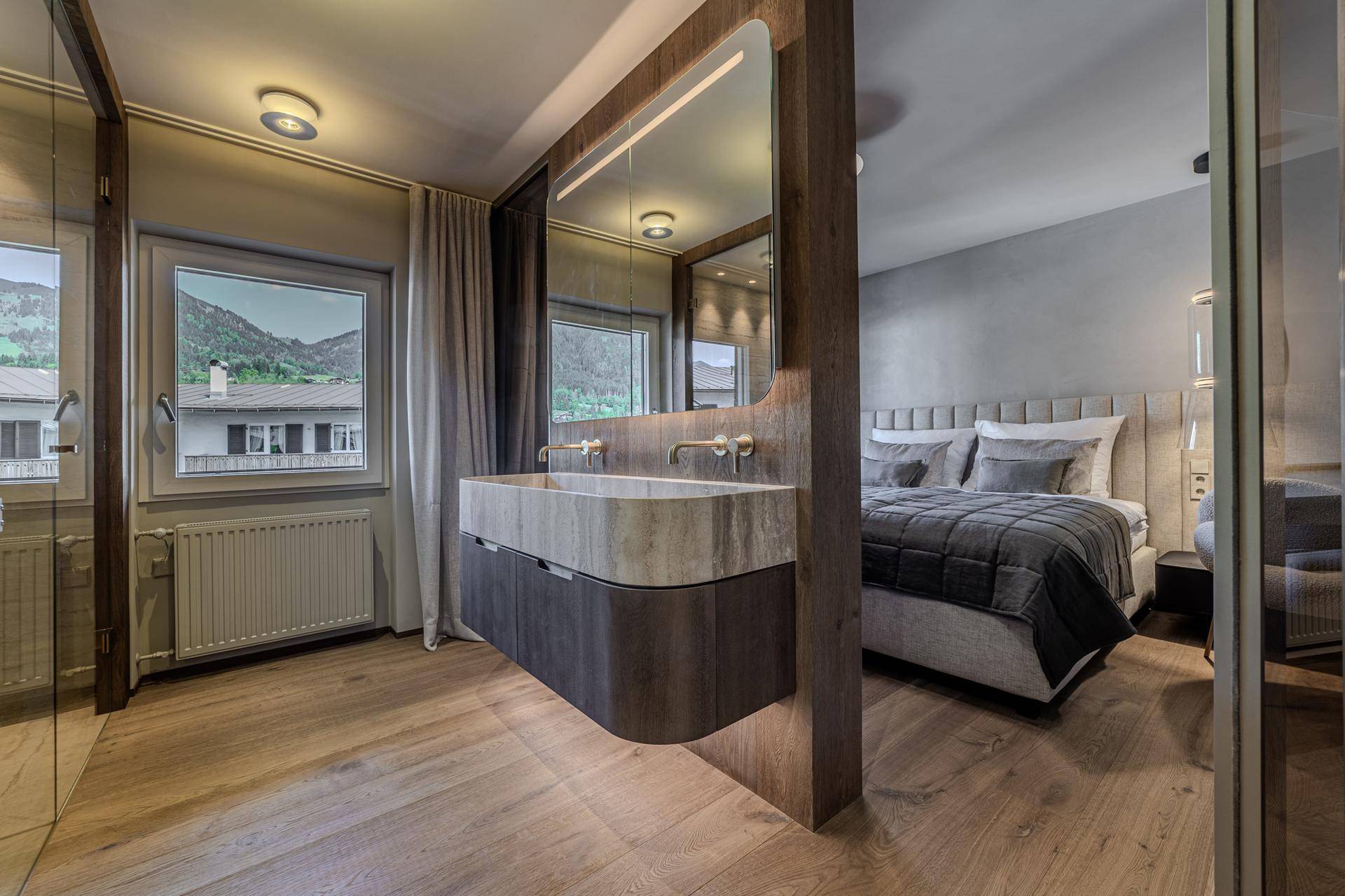 Stilvolles Badezimmer mit Doppelwaschbecken, großem Spiegel und offenem Übergang zum Schlafzimmer.