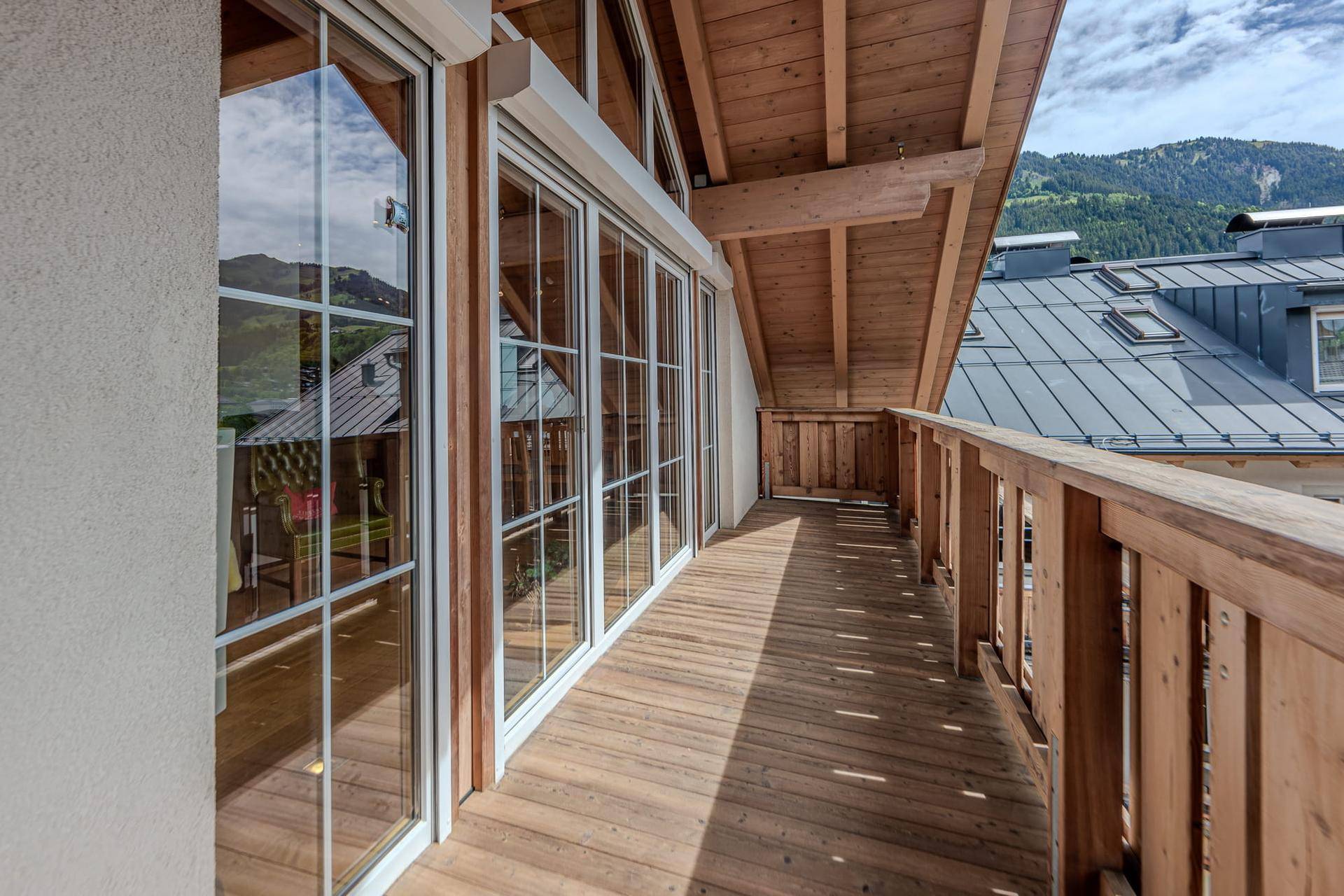 Langer Holzbalkon mit Bergblick und Zugang zu den Innenräumen durch große Fensterfronten.