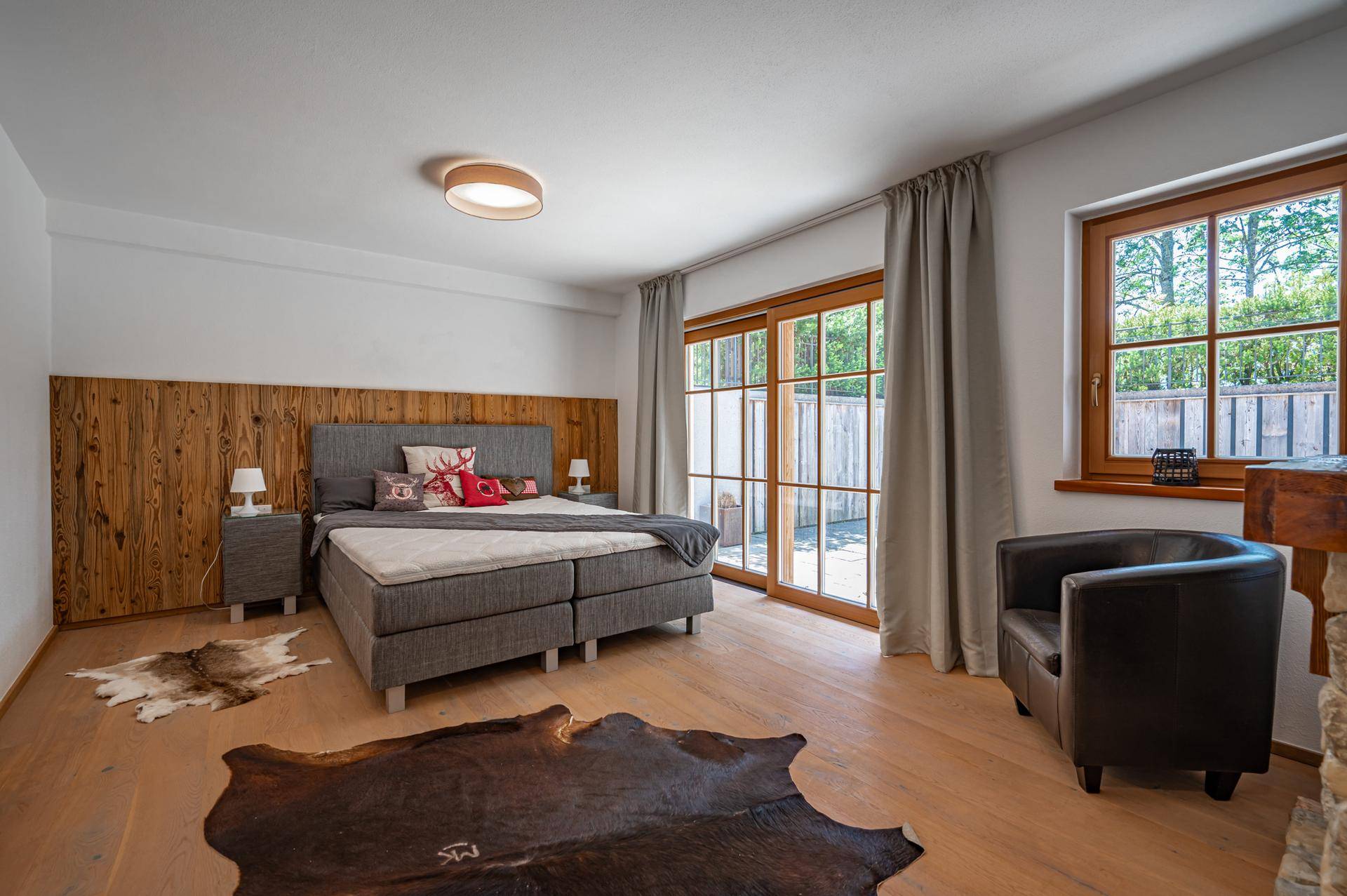 Schlafzimmer im alpinen Stil mit Holzwandverkleidung, Doppelbett und Zugang zu einem Außenbereich.
