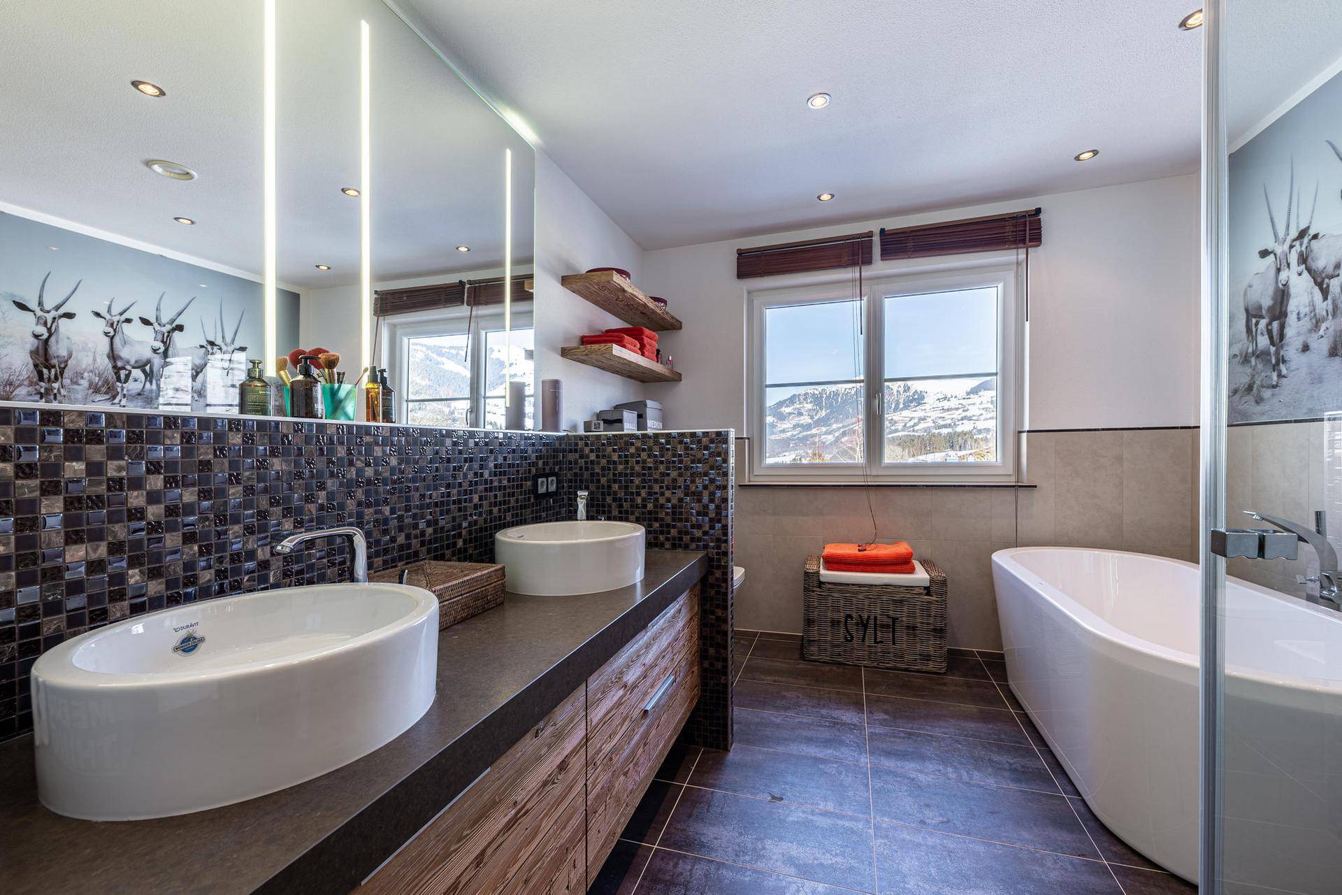 Modernes Badezimmer mit Doppelwaschbecken, freistehender Badewanne und Bergblick durch das Fenster.