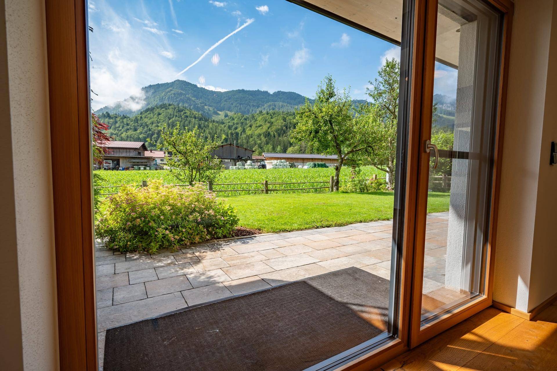 Terrasse mit Steinplatten und Zugang zum Garten, umgeben von grüner Natur und Bergblick.