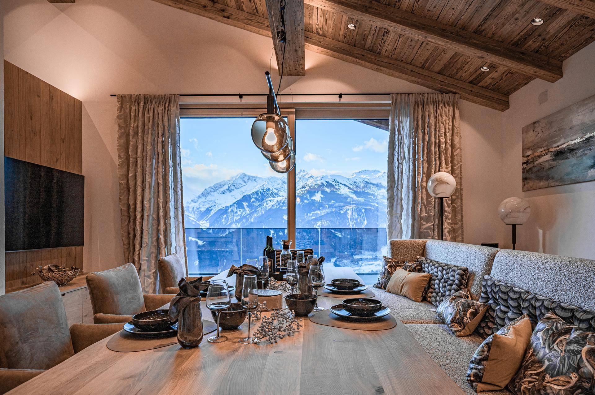 Eleganter Essbereich mit Holztisch, bequemer Sitzbank und direktem Blick auf die schneebedeckten Berge.