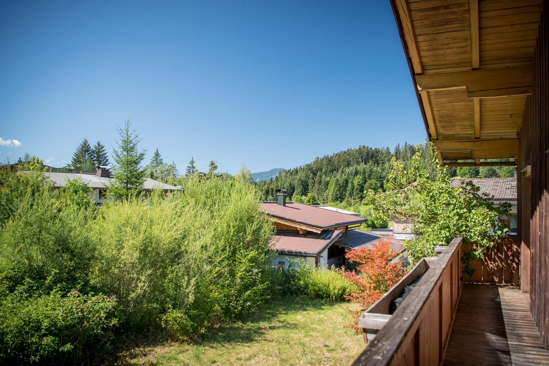 Holzbalkon mit weitem Blick über grüne Bäume und die umliegende Berglandschaft.