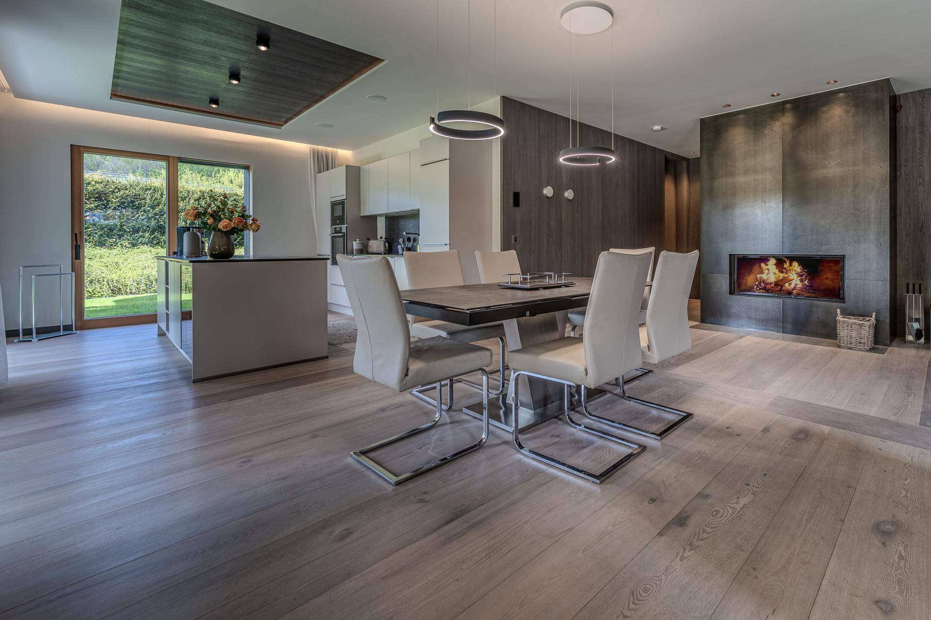 Moderner Essbereich mit Holzboden, Kamin und offener Küche im Hintergrund.