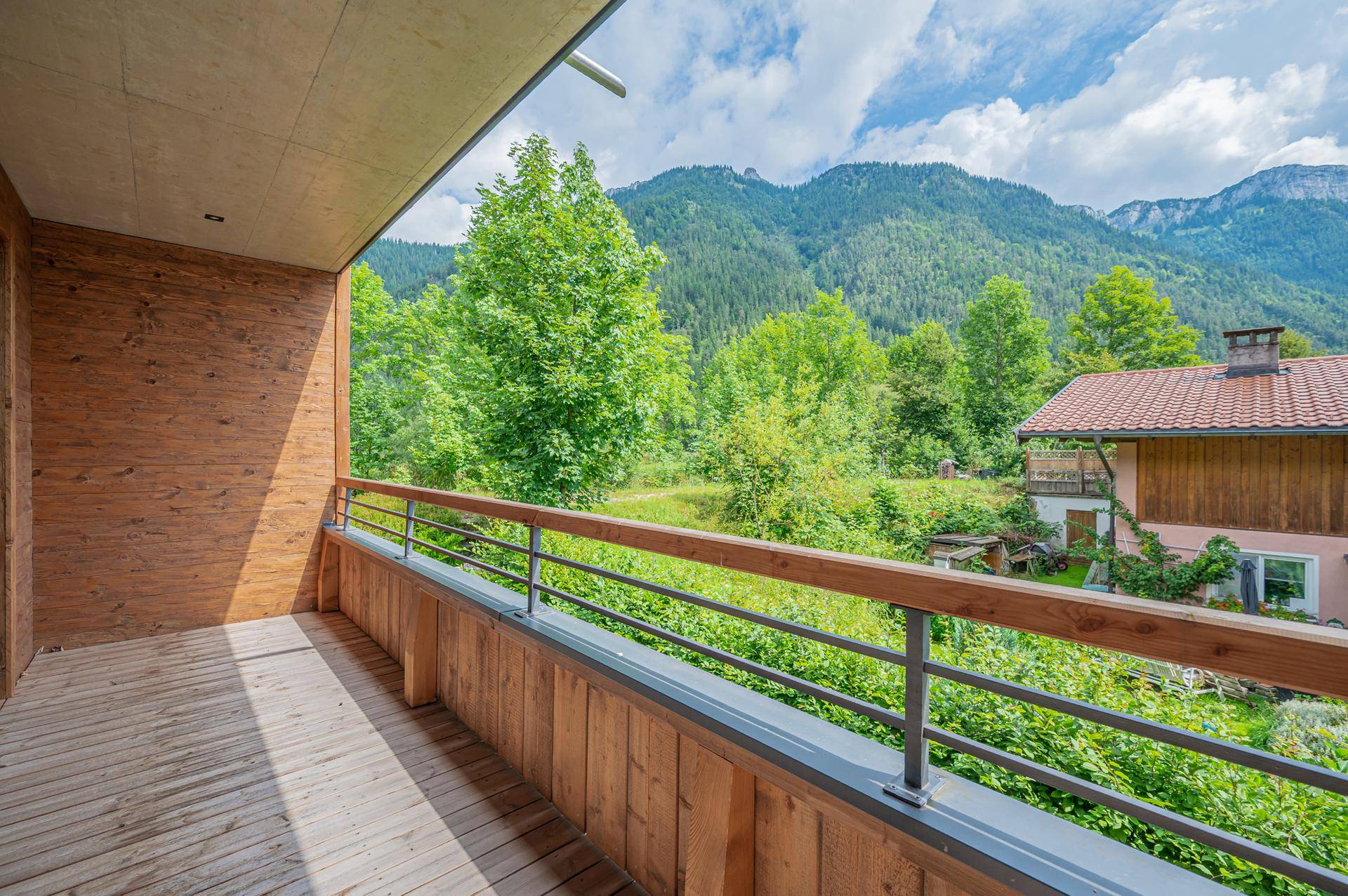 Geräumiger Balkon mit Holzboden und Geländer, bietet einen weiten Blick auf die Berge und grüne Natur.