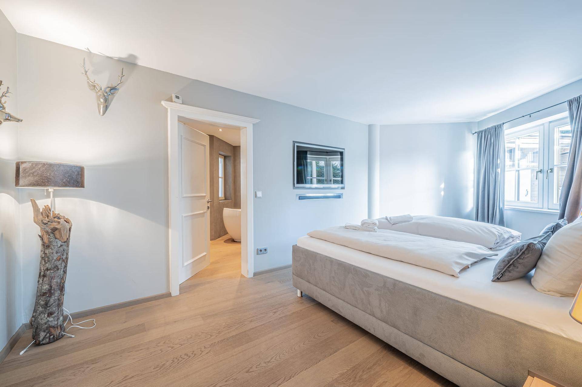 Schlafzimmer mit Holzboden, TV und Zugang zu einem modernen Badezimmer.