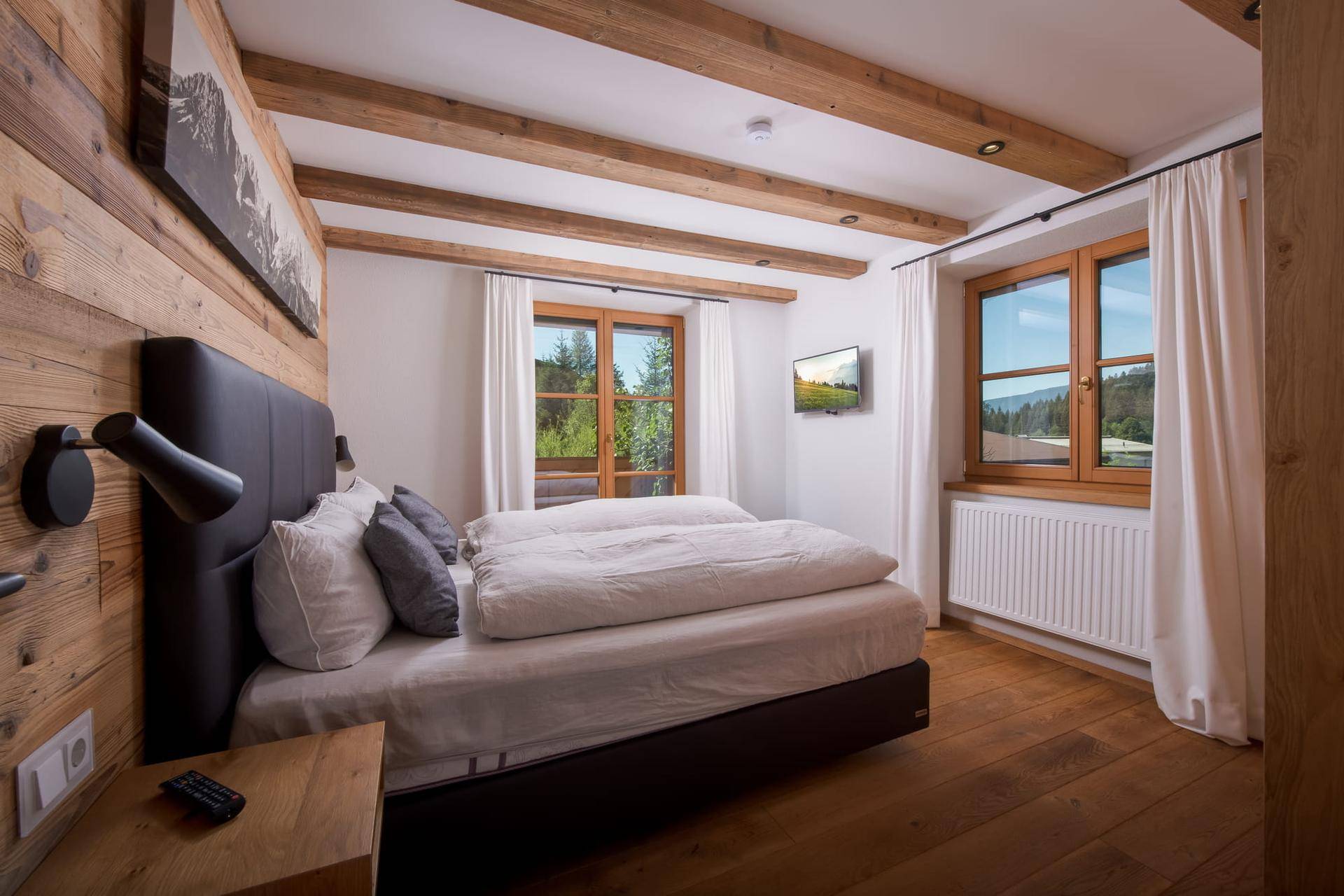 Schlafzimmer im alpinen Stil mit Holzwänden, sichtbaren Deckenbalken und Fenstern zur Natur.