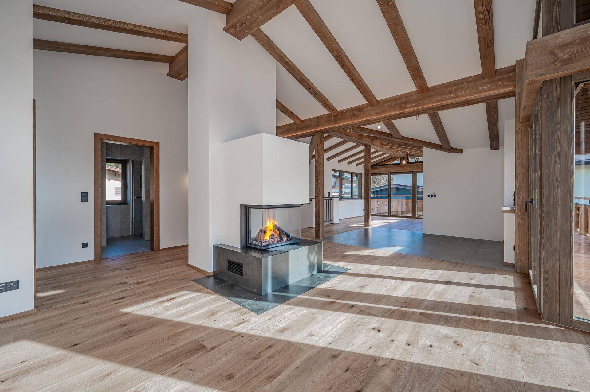 Geräumiger Wohnbereich mit offenem Kamin, sichtbaren Holzbalken und viel Tageslicht.