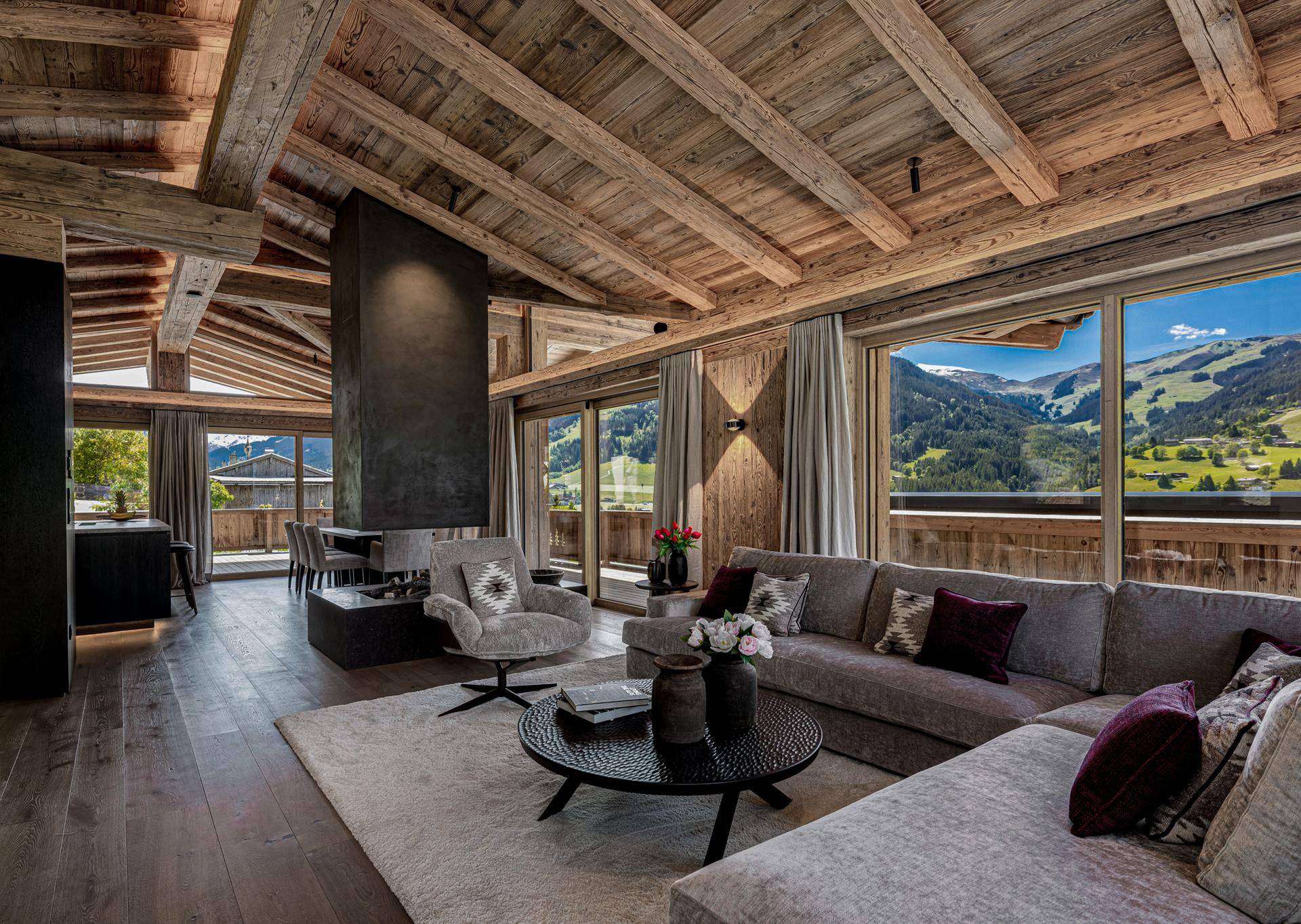 Gemütliches Wohnzimmer mit modernem Kamin, Holzbalken und weitem Blick auf die umliegende Berglandschaft.