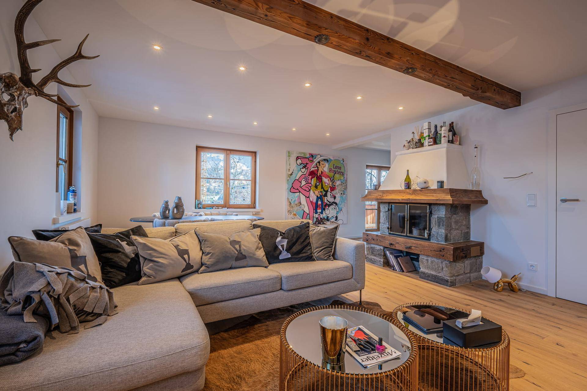 Gemütliches Wohnzimmer mit Ecksofa, Steinkamin und rustikalen Holzbalken an der Decke.