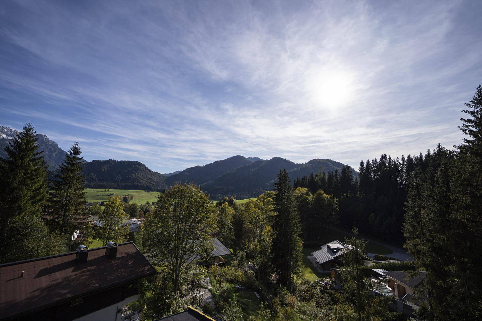 Weitläufiger Blick über grüne Hügel, Wälder und ein Tal mit Häusern unter blauem Himmel.