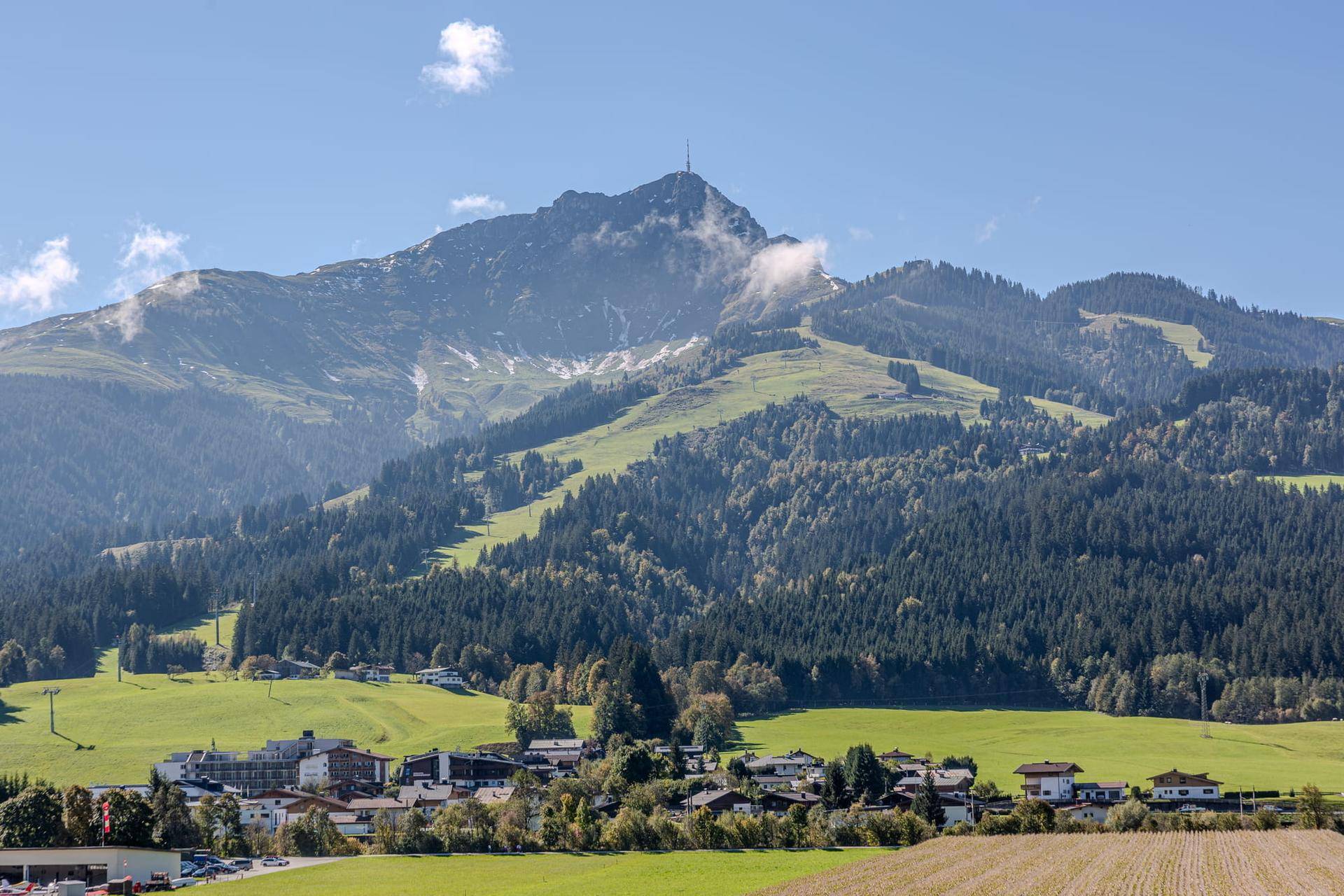 Panoramablick auf eine majestätische Berglandschaft mit bewaldeten Hängen und einem malerischen Dorf am Fuße.