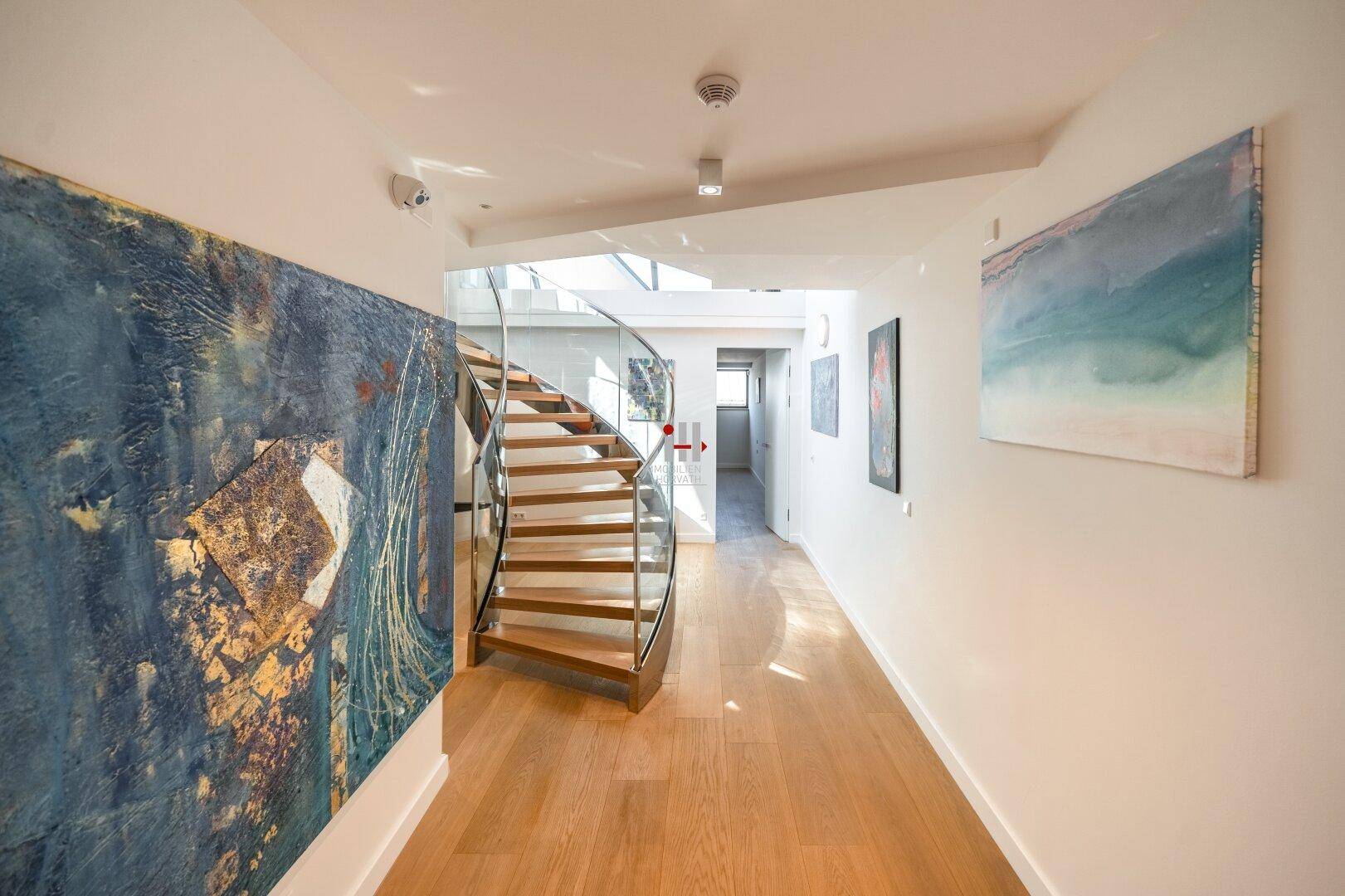 Heller Flur mit Holzboden und moderner Kunst, der zu einer eleganten Wendeltreppe führt.