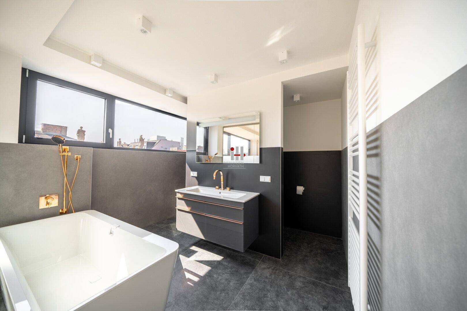 Modernes Badezimmer mit Badewanne, Doppelwaschbecken und großen Fenstern für viel Tageslicht.