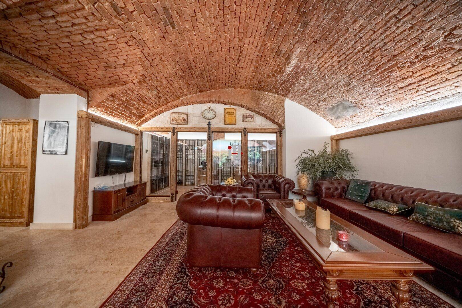 Gemütlicher Wohnbereich im Keller mit Ziegelgewölbe, Ledersofas und traditionellem Teppich.